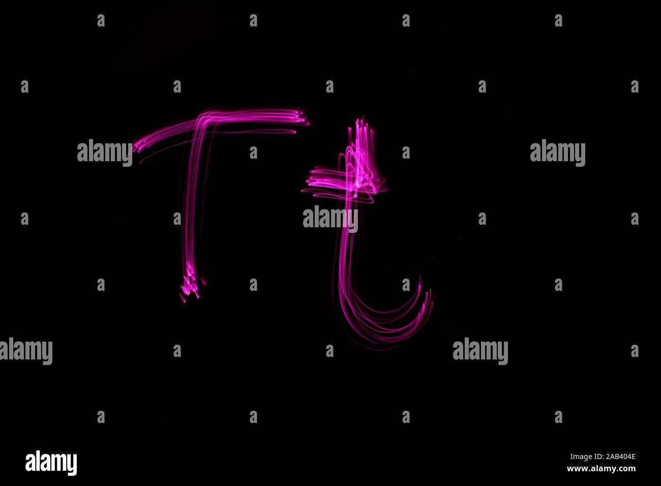 Une longue exposition photo de la lettre t en couleur néon rose, en majuscules et minuscules, motif de lignes parallèles sur un fond noir. Banque D'Images