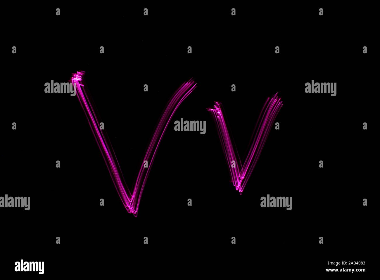 Une longue exposition photographie de la lettre v en couleur néon rose, en majuscules et minuscules, motif de lignes parallèles sur un fond noir. Banque D'Images