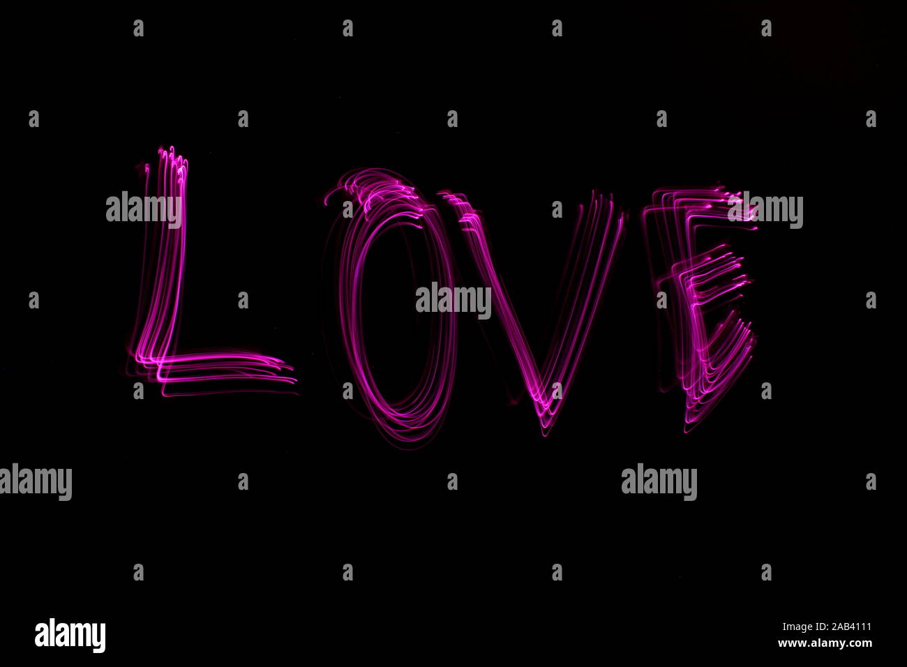 Longue exposition de photographie le mot 'Amour' en couleur néon rose dans un abrégé swirl, motif de lignes parallèles sur un fond noir. Peinture de lumière Banque D'Images