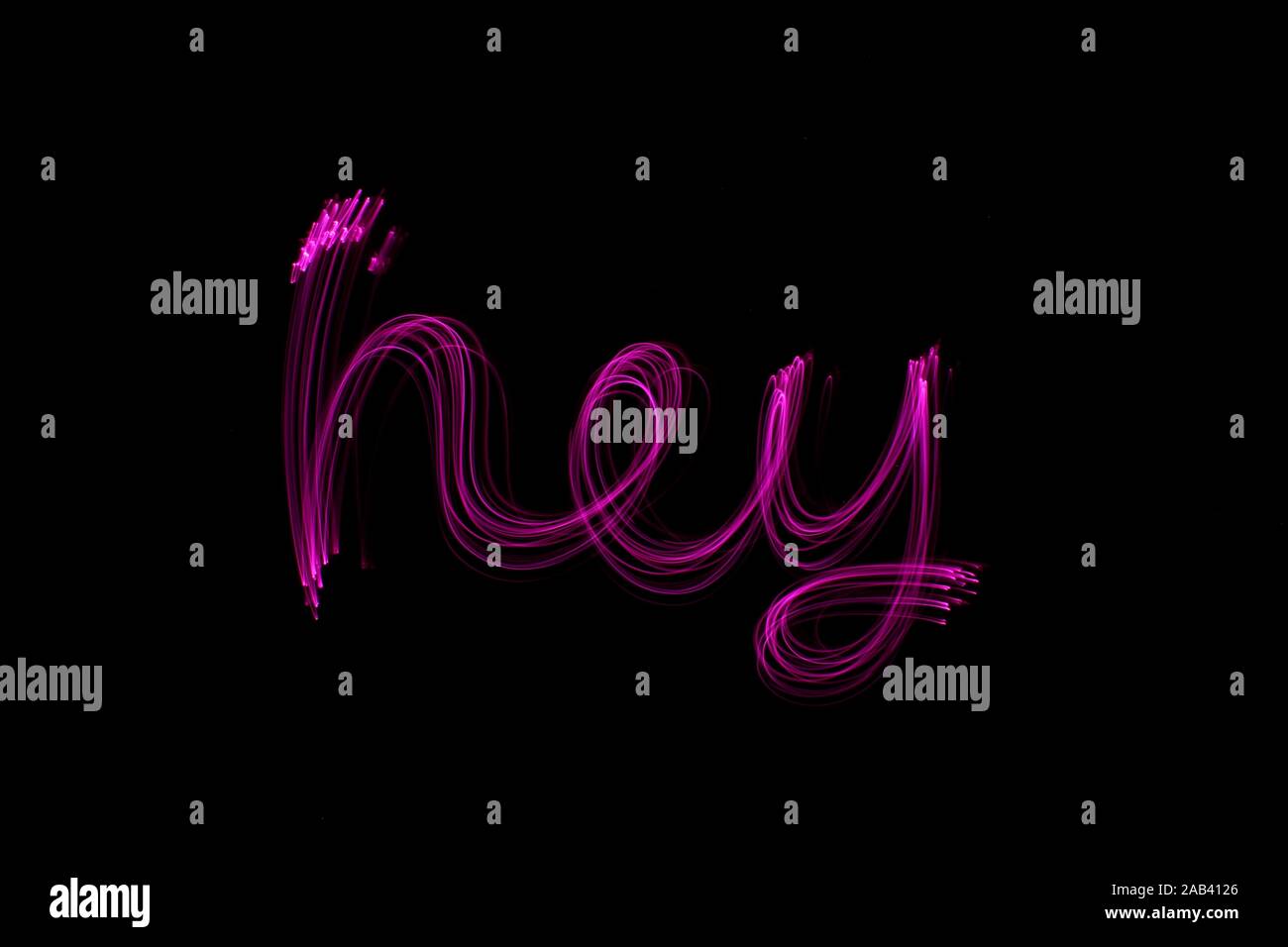 Une longue exposition photographie du mot 'hey' en couleur néon rose dans un abrégé swirl, motif de lignes parallèles sur un fond noir. Peinture de lumière Banque D'Images