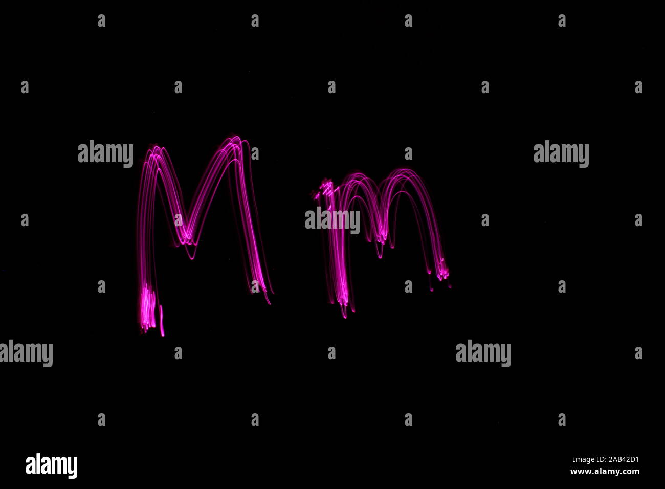 Une longue exposition photo de la lettre m en couleur néon rose, en majuscules et minuscules, motif de lignes parallèles sur un fond noir. La lumière pa Banque D'Images