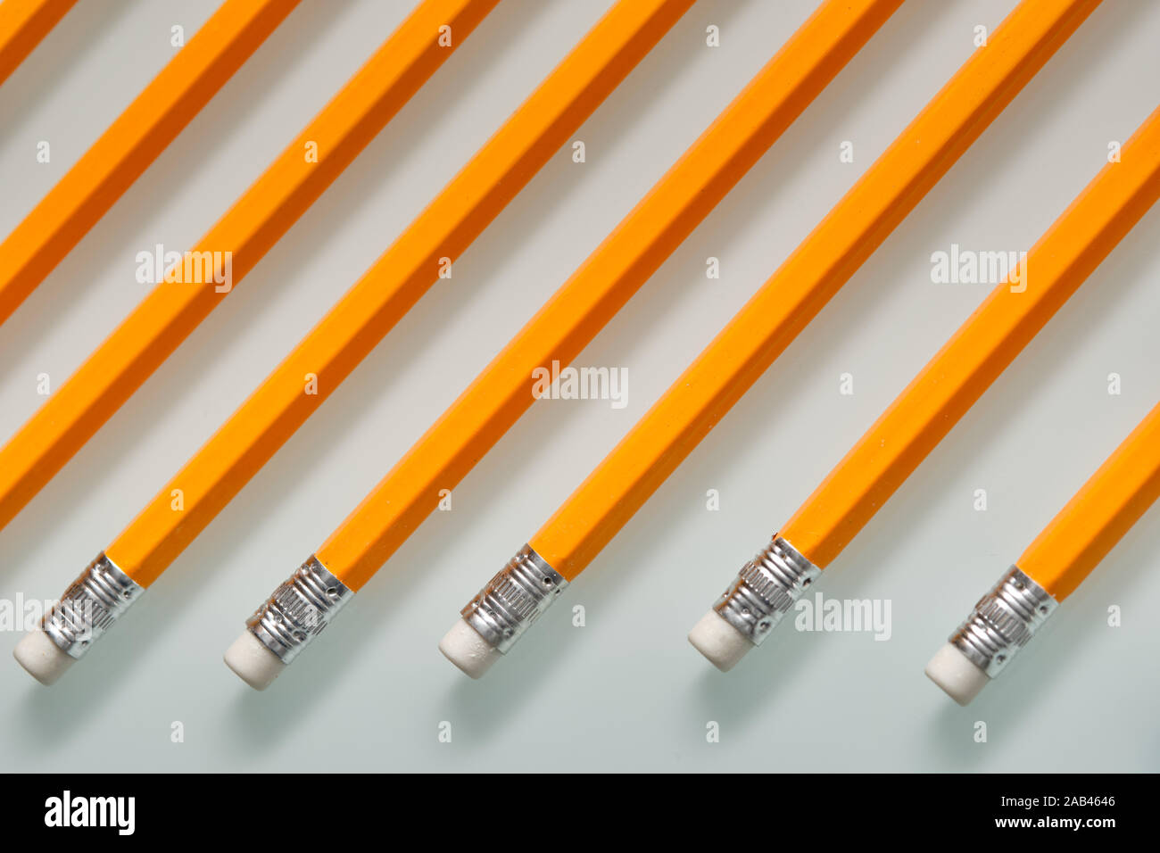 Arrière-plan avec un motif composé d'un gros plan d'une rangée de crayons de plomb blanc orange avec des caoutchoucs sur la fin est posé sur une plaque de verre blanc. Banque D'Images