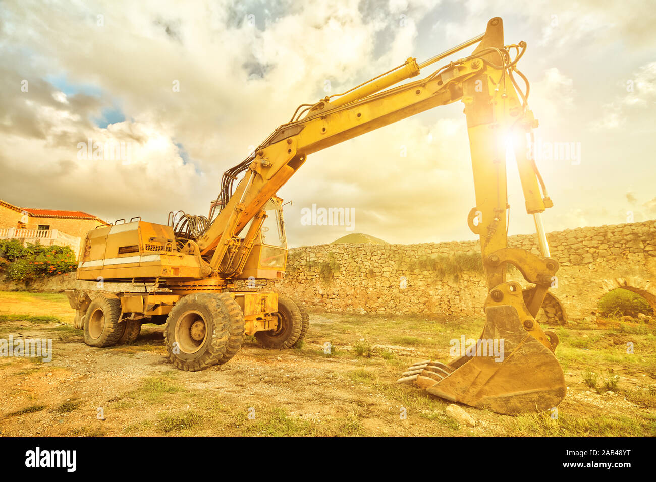 Vue latérale d'excavatrice jaune pour les travaux de construction le long de la route dans un chantier de construction au coucher du soleil. Les travaux en cours, une machine industrielle. Banque D'Images