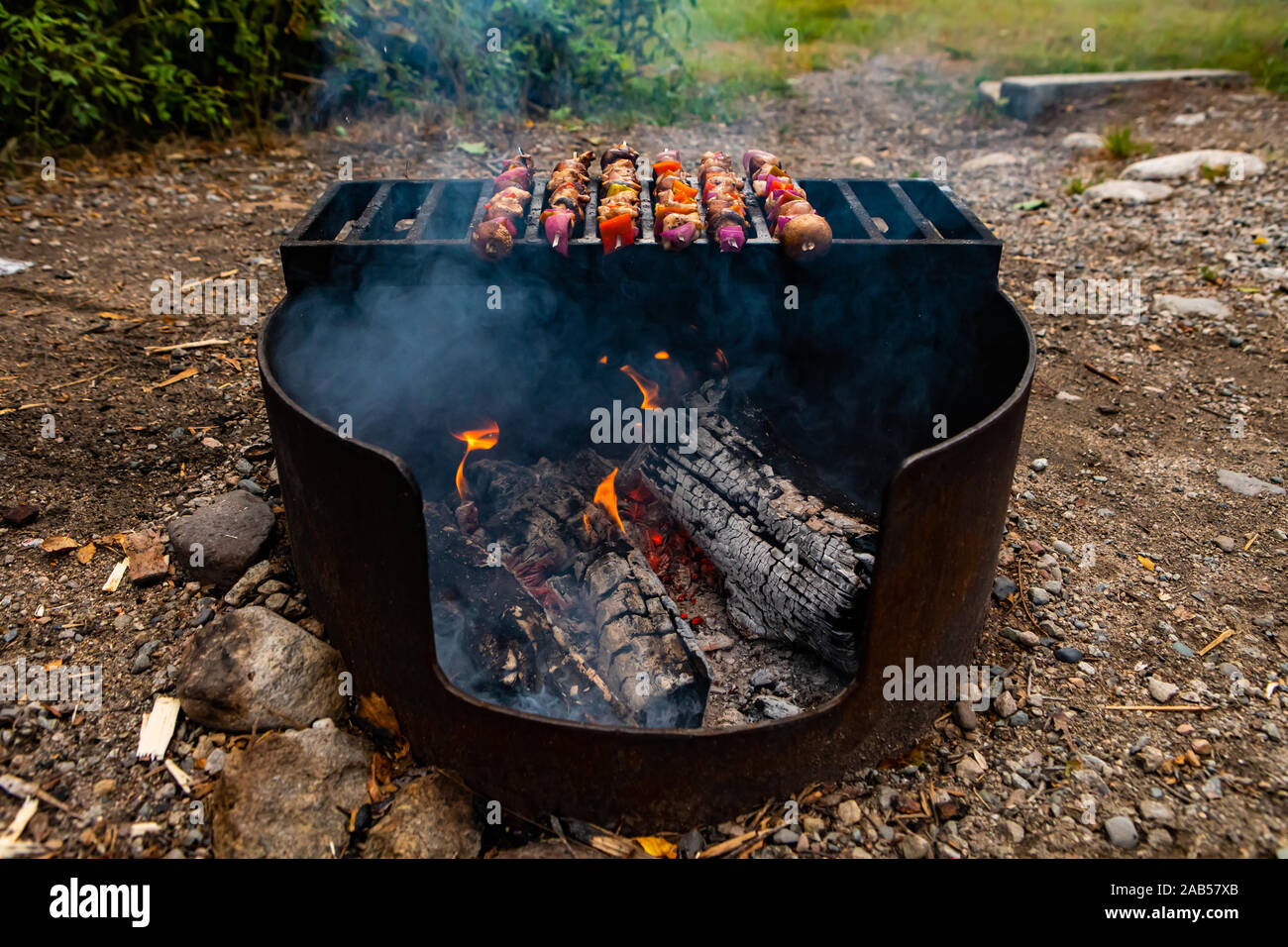 Focus sélectif du grand barbecue fait maison avec la combustion du bois à  l'intérieur de la cuisson des brochettes de viande lentement au-dessus de  lui dans un paysage de la nature l'extérieur