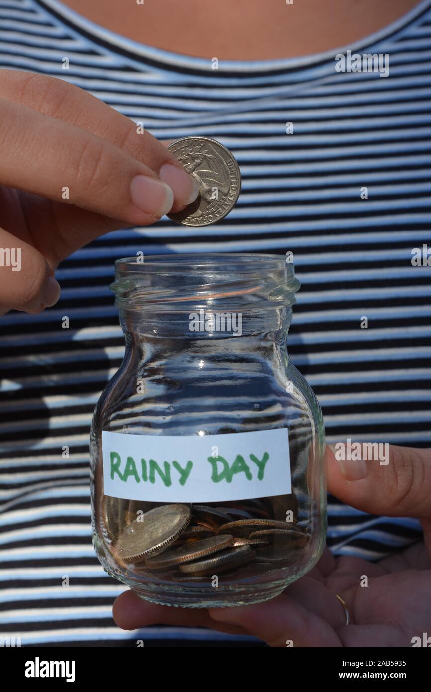 Épargner pour un jour de pluie, femme de mettre une pièce dans un pot en verre à Banque D'Images