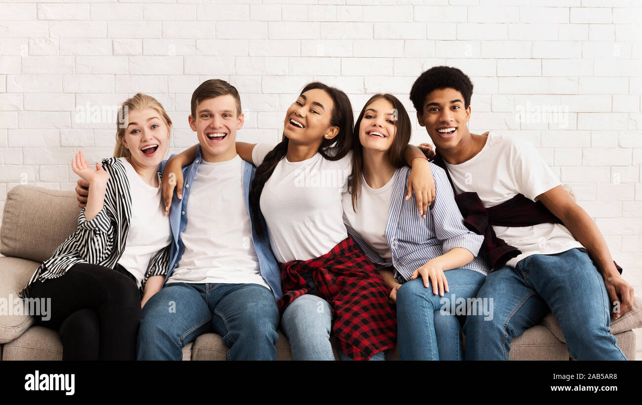 Amis adolescents assis sur un canapé et enlacés, smiling to camera Banque D'Images