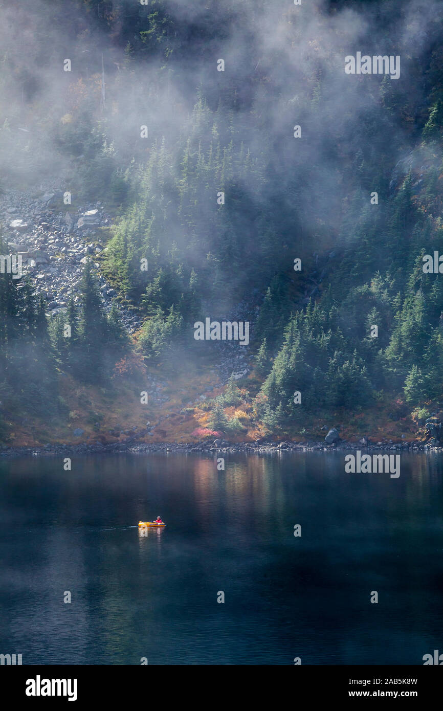 Un homme dans un petit radeau pneumatique de l'aviron sur le lac de la neige au-dessus de Snoqualmie Pass dans la partie centrale de la chaîne des Cascades dans l'État de Washington, USA. Banque D'Images