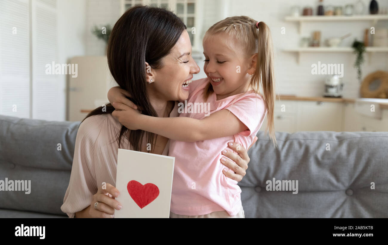 Cheerful maman embrassant kid fille holding carte postale avec coeur rouge Banque D'Images