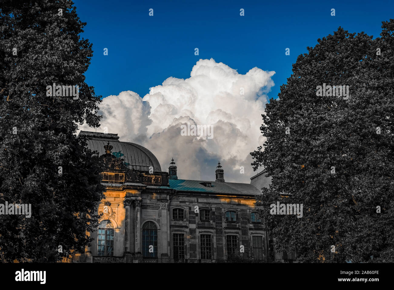 La formation de nuages cumulus blanc dominant dans un beau ciel bleu sur la façade bombée d'un bâtiment historique entouré par les arbres verts feuillus Banque D'Images