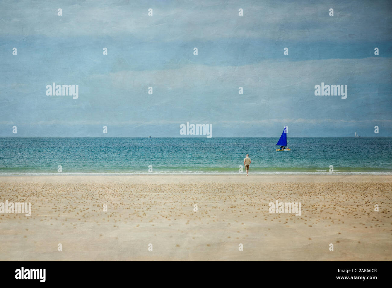 Image texturée d'un homme debout sur une plage donnant sur la mer, avec un bateau à voile bleu qui passe. Jersey, Channel Islands. Banque D'Images