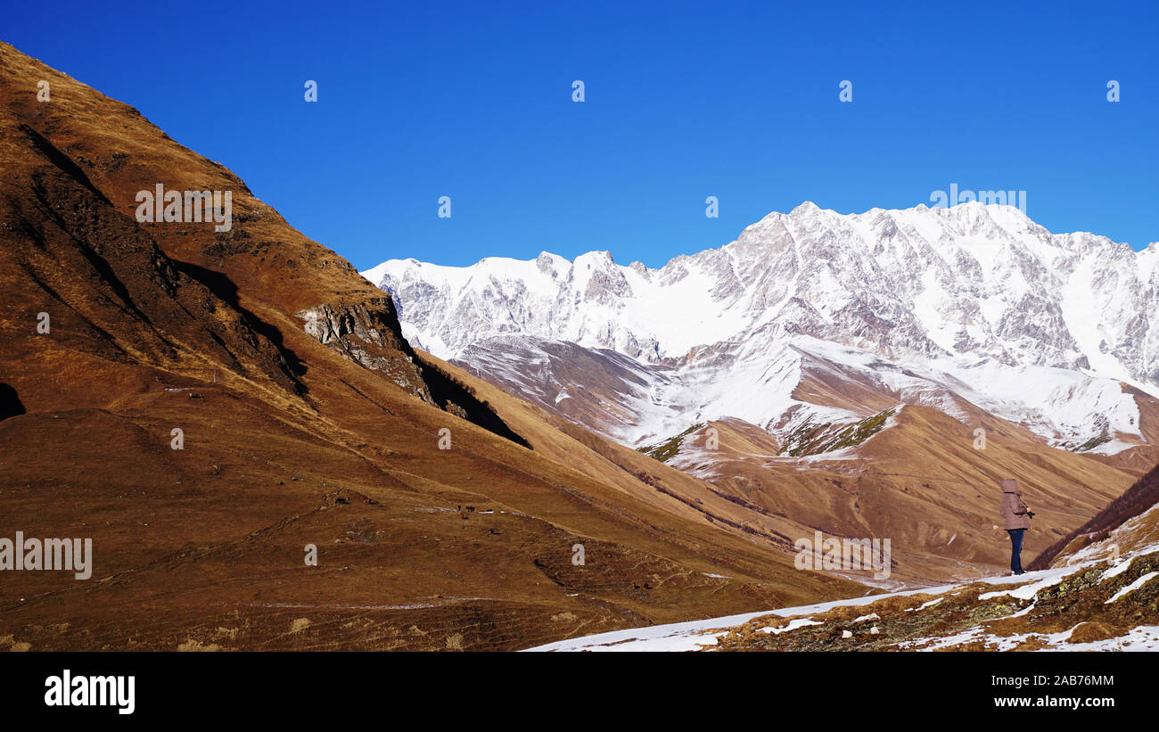 Une fille avec une caméra est la prise de vue. Paysage de montagne panorama. Majestueux sommets de montagnes couvertes de neige contre un ciel bleu. Banque D'Images