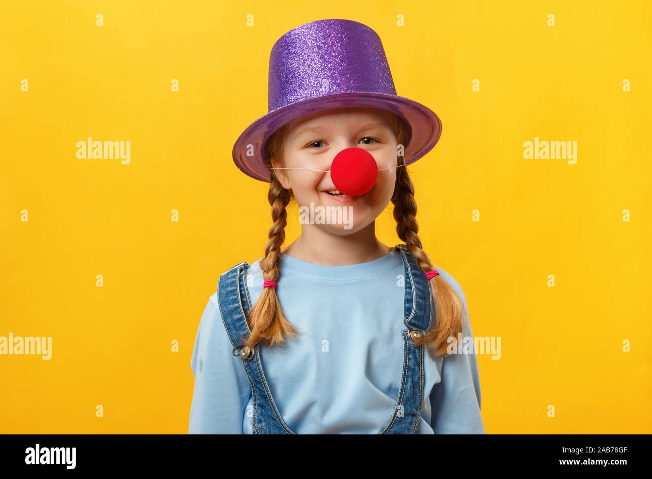 Clown enfant drôle, chapeau et un nez rouge. Petite fille joyeuse sur un fond jaune. Le 1er avril. April Fools Day. Copier l'espace. Banque D'Images