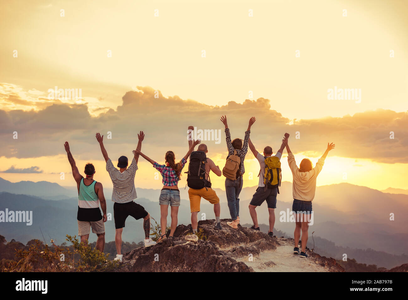 Groupe d'amis heureux se tient avec les bras levés au coucher du soleil sur la montagne et bénéficie d''coucher du soleil Banque D'Images