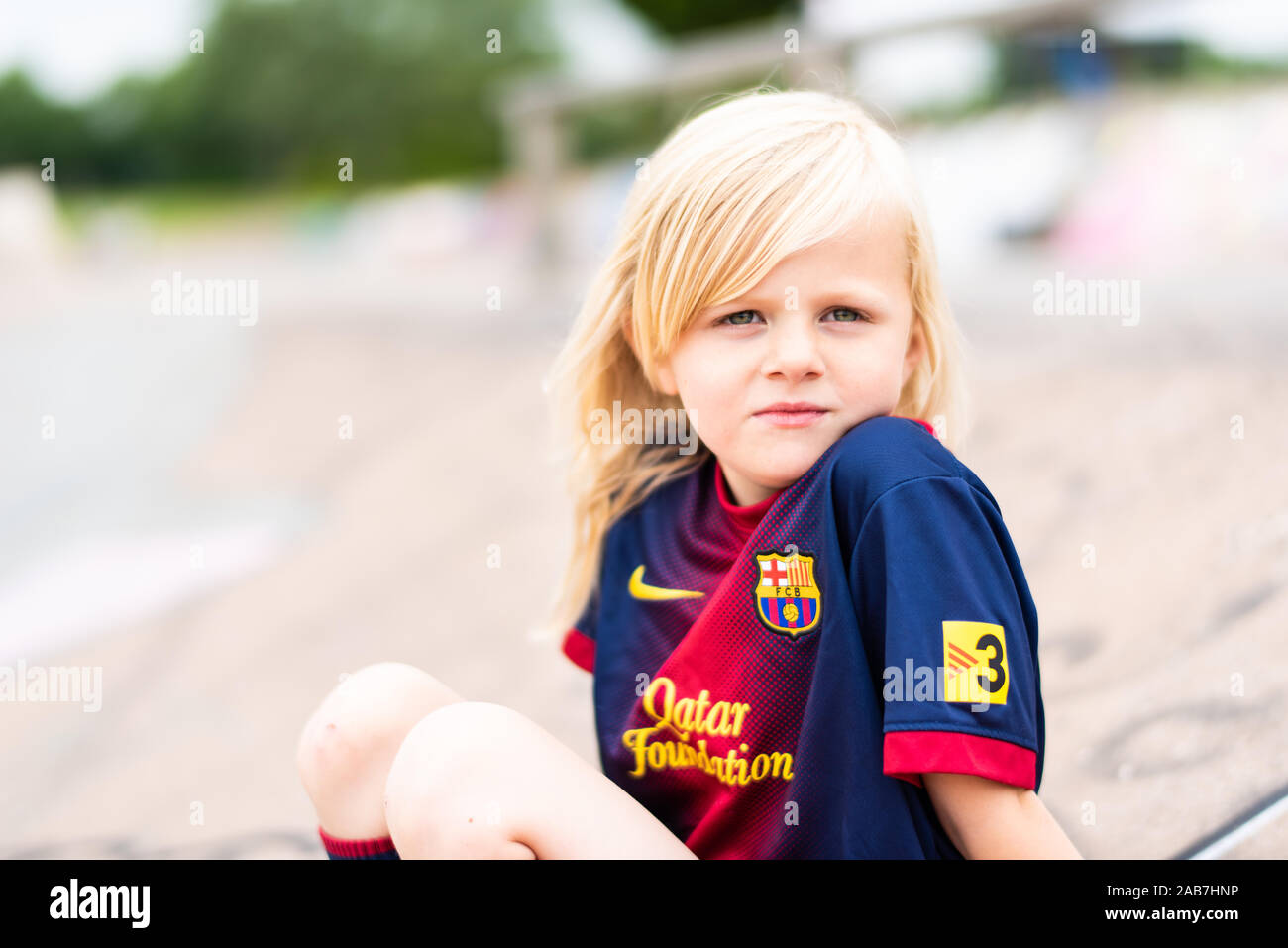 Une jolie, jolie petite fille aux cheveux blonds portant un maillot de foot en pleine réflexion alors qu'il était assis à l'extérieur dans la campagne britannique Banque D'Images