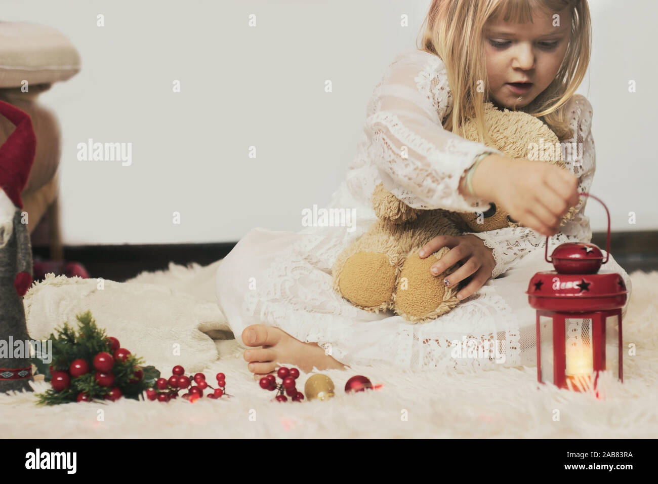 Petite fille assise sur le tapis, avec son ours en peluche, jouant avec décoration de Noël Banque D'Images