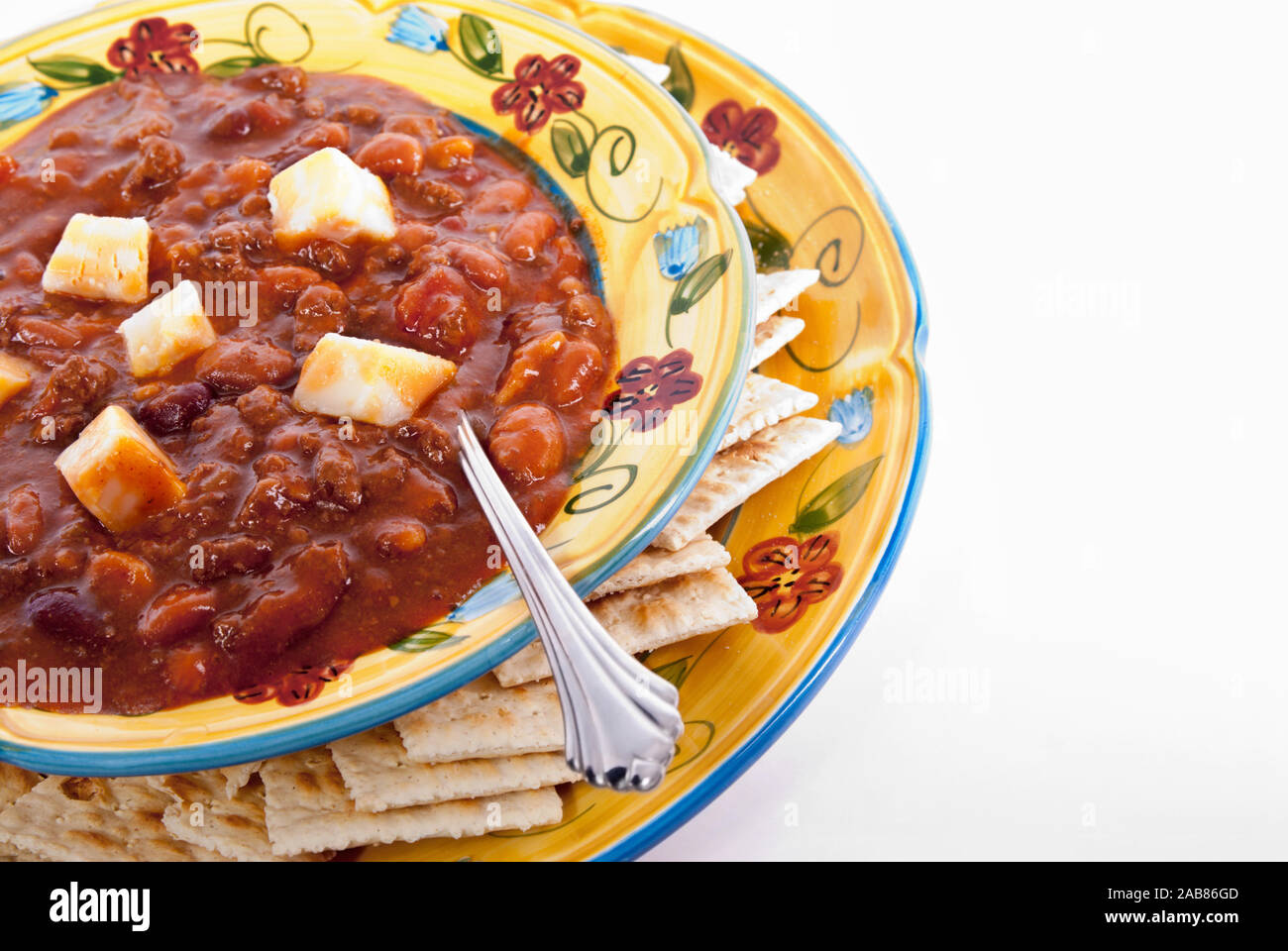 Un bol de chili fait maison servi avec des cubes de fromage Colby et saltine crackers. Isolé sur fond blanc. Banque D'Images