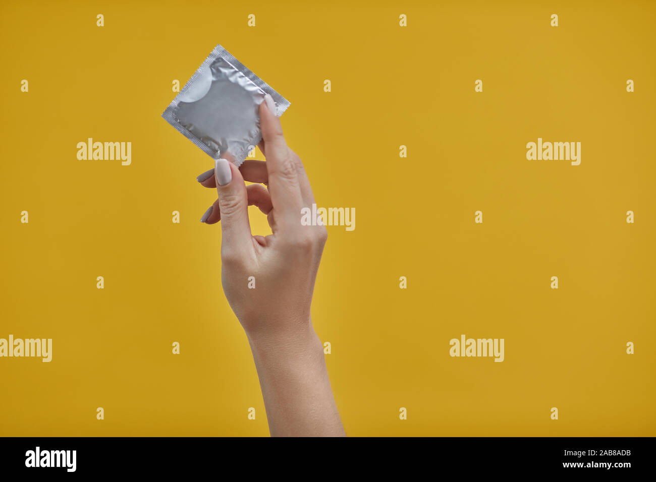 Femme hands holding condom sur fond jaune Banque D'Images