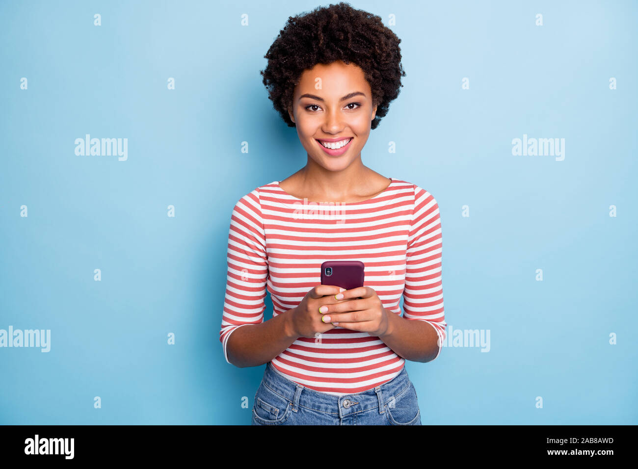 Photo de jolie peau sombre dame holding téléphone mains lecture nouveau poster des commentaires reposts aime porter des jeans pull rayé décontracté couleur bleu isolé Banque D'Images