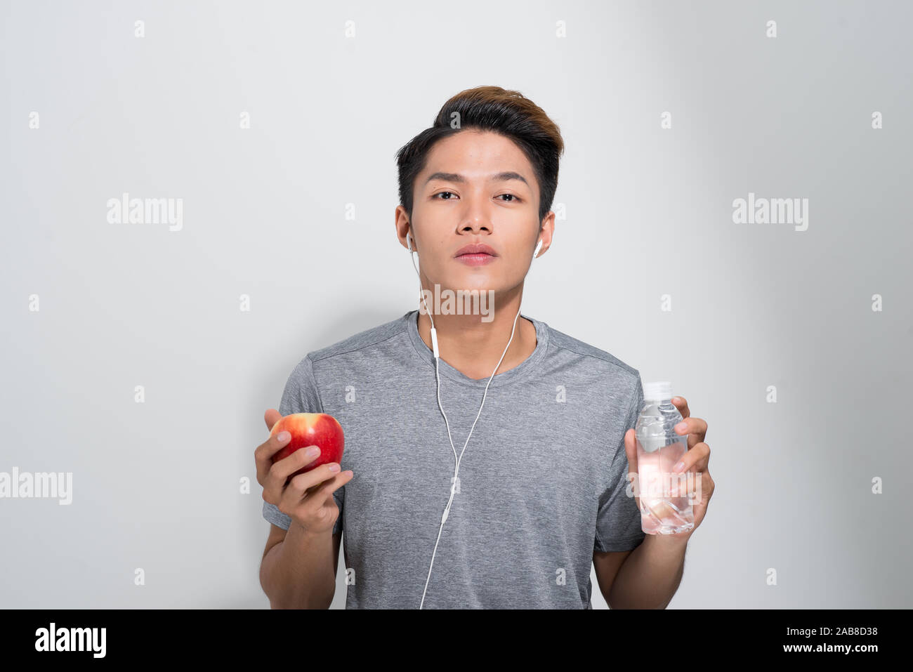 Jeune homme fit sourire avec Apple et une bouteille d'eau contre une salle de sport Banque D'Images