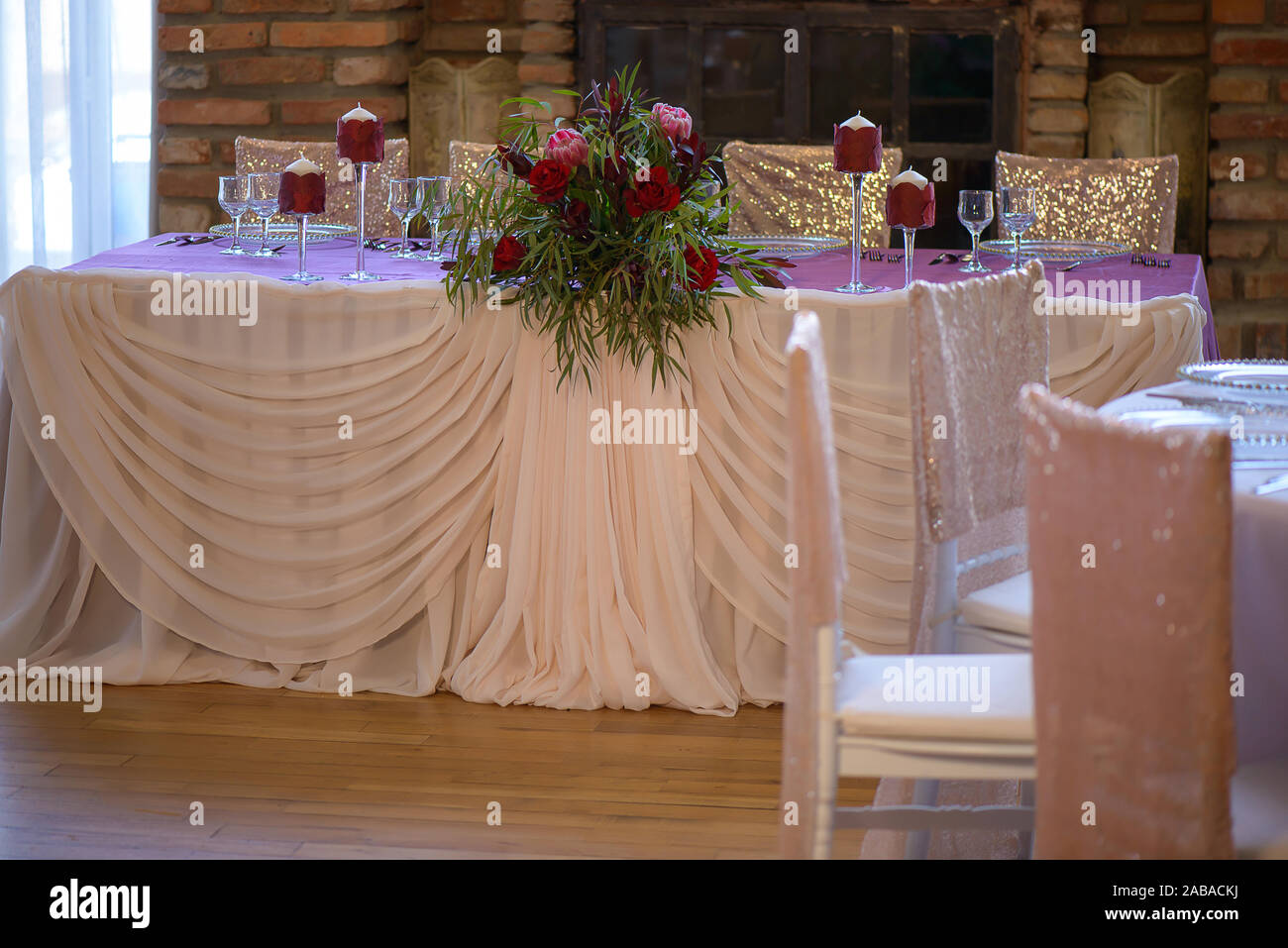 De belles roses rouges frais et de verdure centre situé sur une table de fête avec des verres et des bougies et drapée dans un voile soyeux Banque D'Images