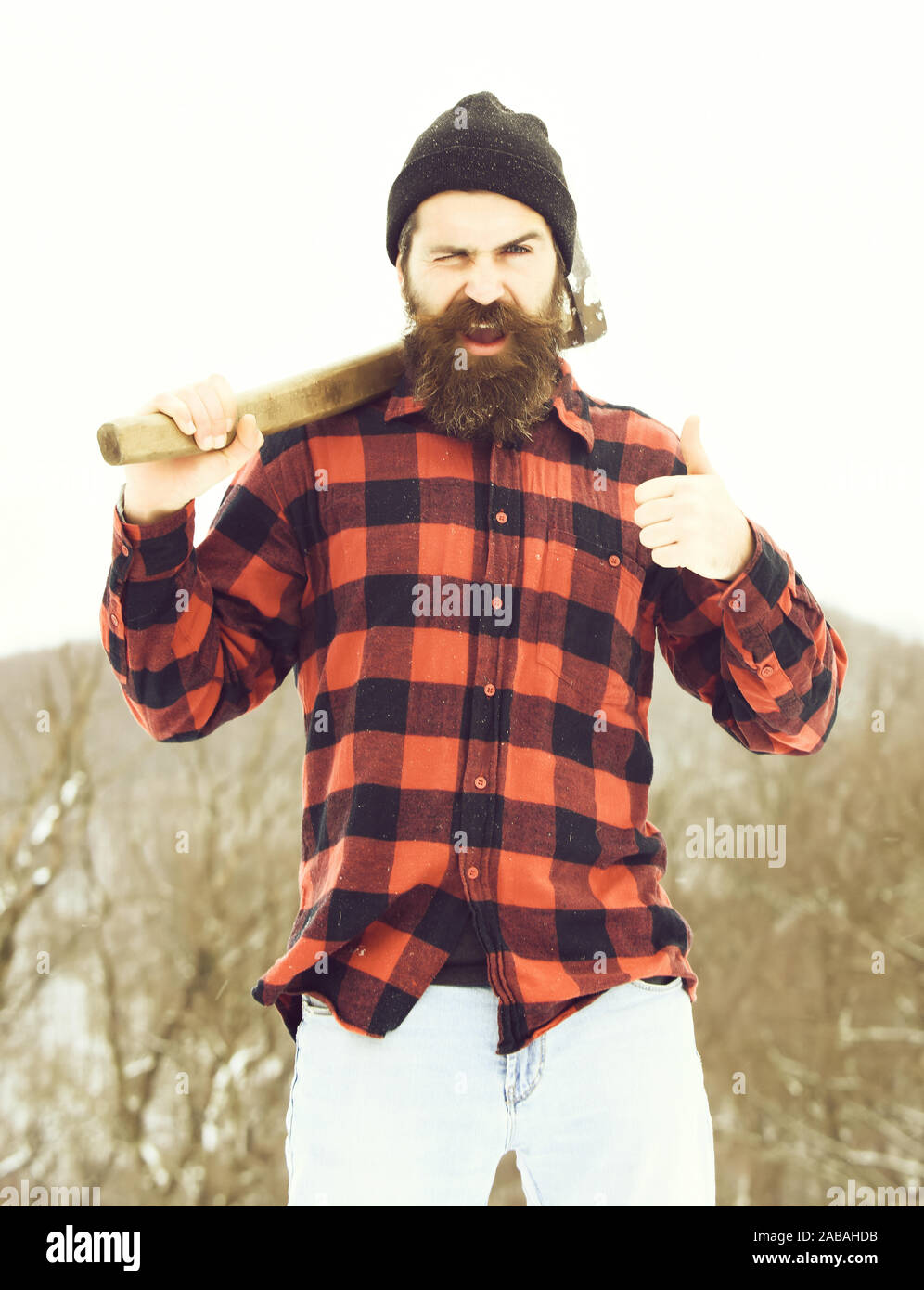 L'homme excité ou bûcheron, hipster barbu, avec barbe et moustache en  chemise à carreaux rouge avec ax donne à coup de gestes dans la forêt  enneigée sur journée d'hiver à l'extérieur, sur
