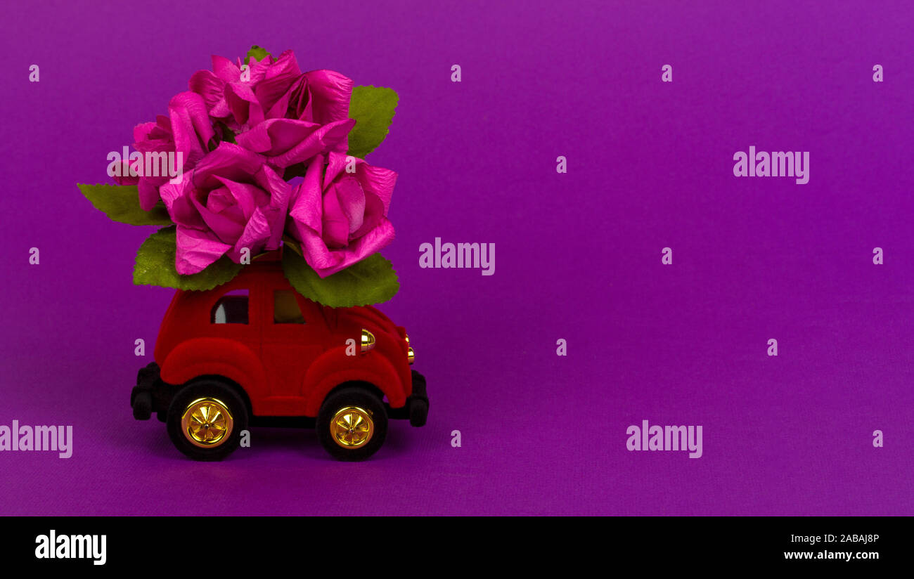 Sochi, Russie - 26 octobre 2019 : velours rouge petite voiture livrer bouquet de fleurs sur fond violet avec copie espace. Carte de Saint-Valentin, birthda Banque D'Images