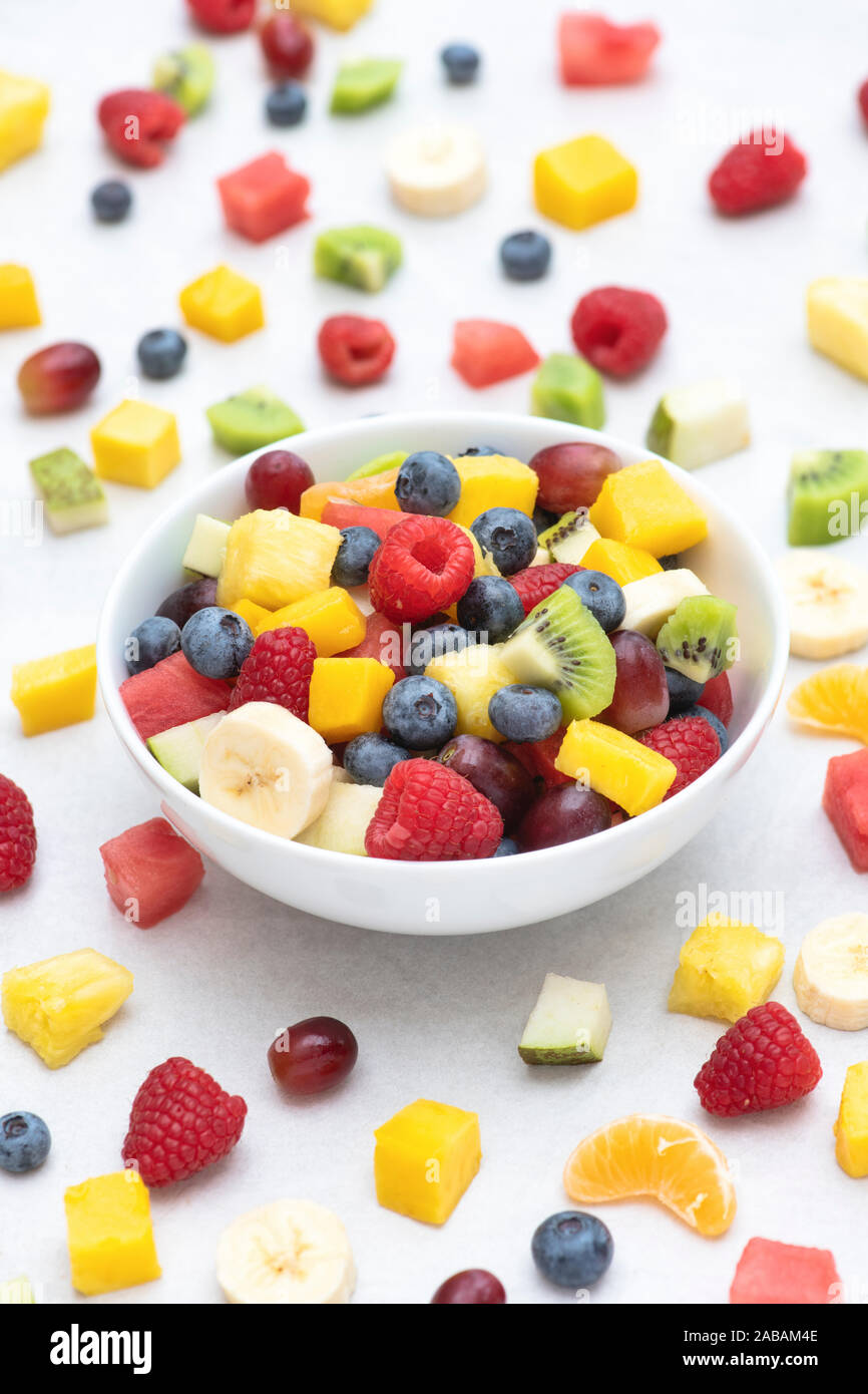 Bol de fruits coupés sur un fond blanc. Comprend des fruits framboises, bleuets, raisins, banane, mangue, ananas, melon, kiwi et poire Banque D'Images