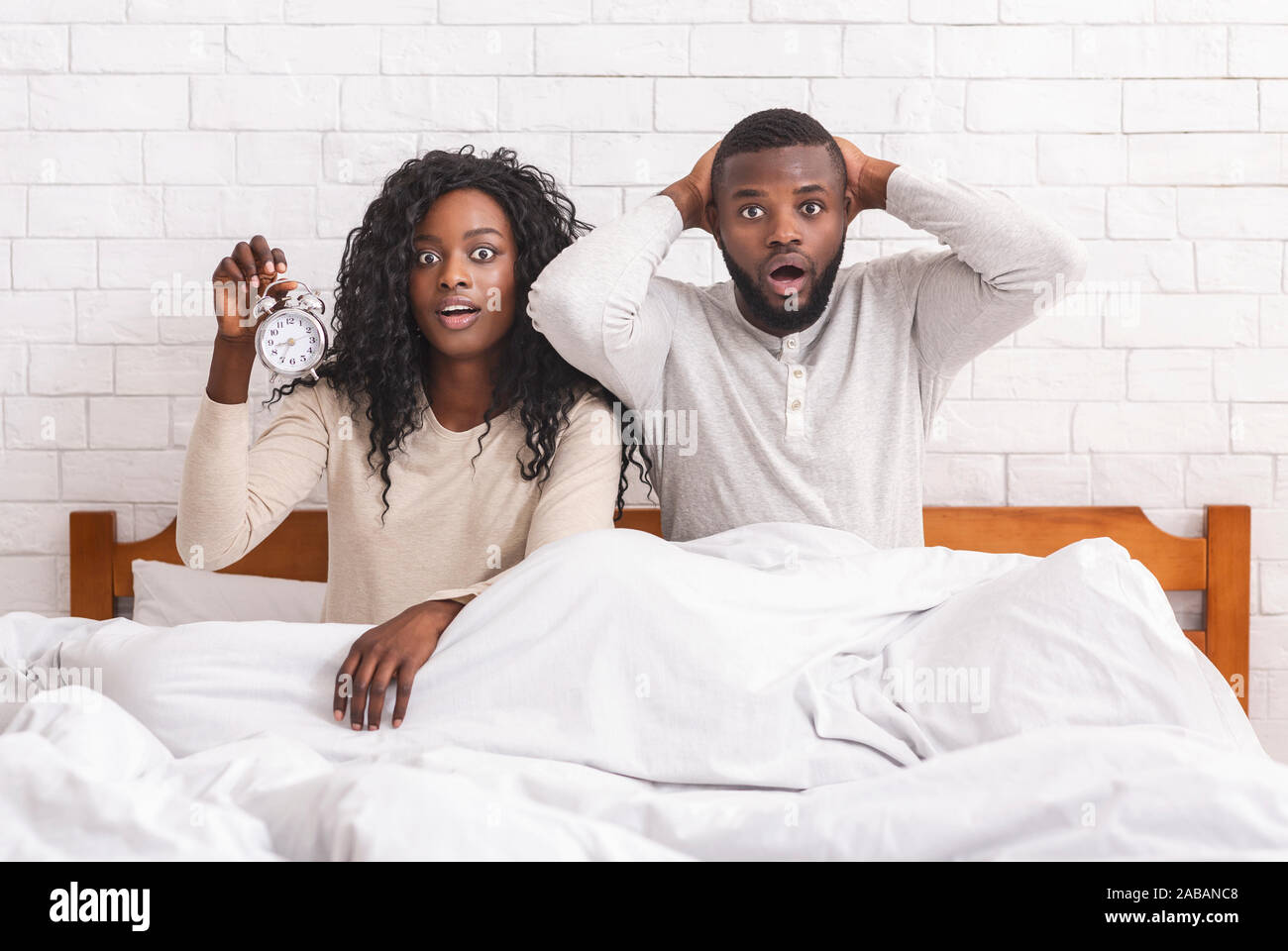 Black couple raté réveil sonner, assis sous le choc au lit Banque D'Images