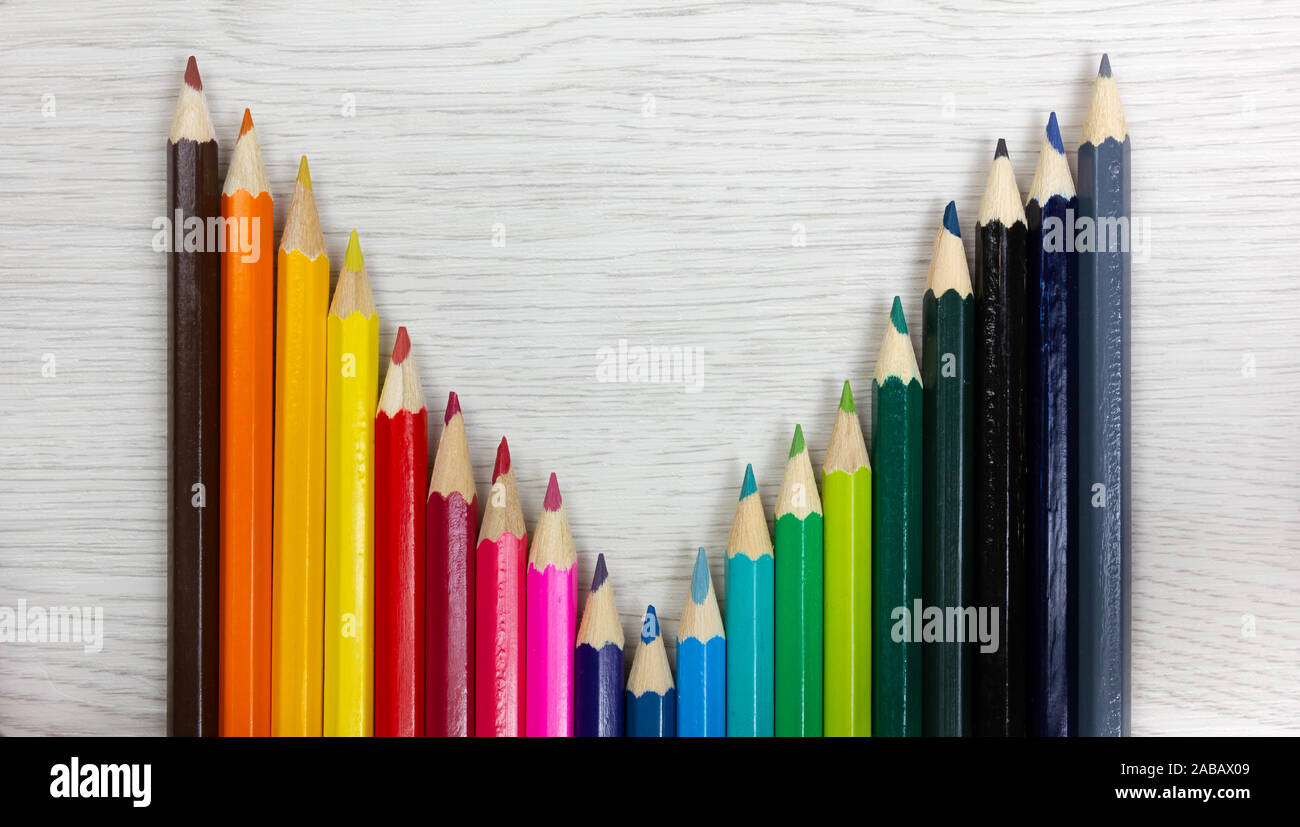 Série de crayons de couleur sur un fond de bois blanc placés de manière à dessiner une courbe Banque D'Images