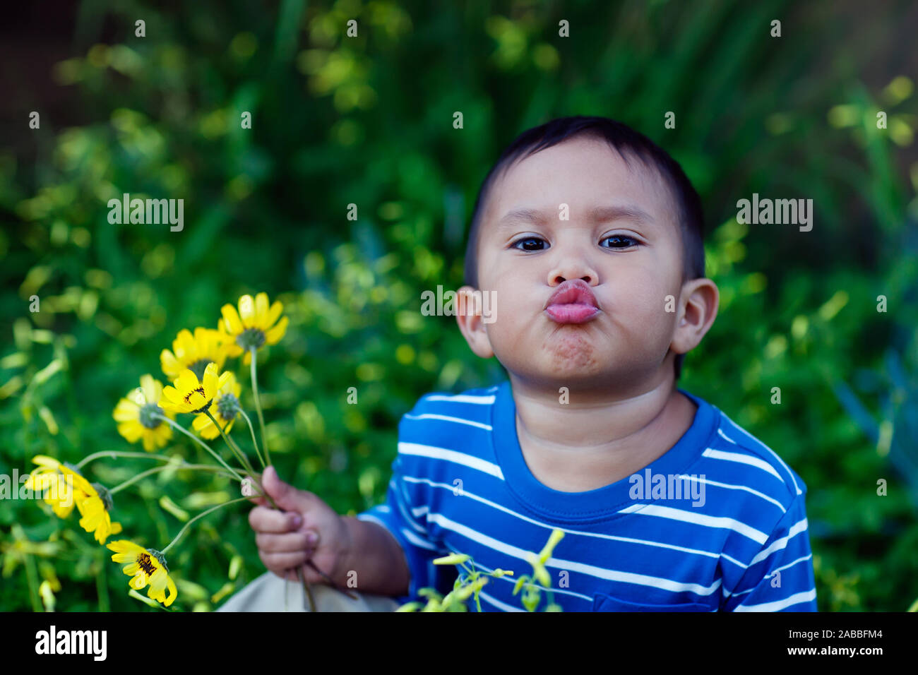 Un jeune enfant tenant un bouquet de fleurs sauvages de Californie, avec des lèvres plissées en donnant des baisers. Banque D'Images