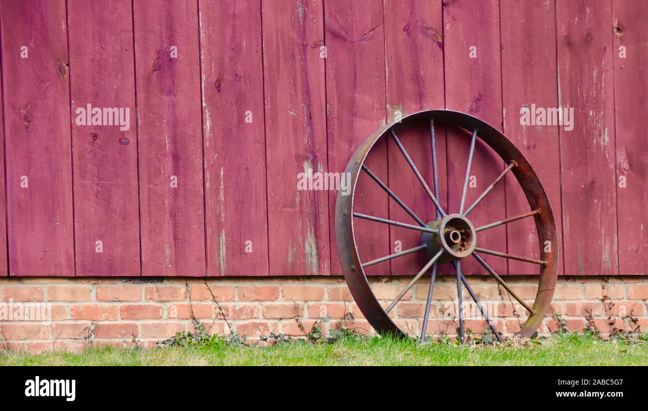 Ancienne ferme la roue du tracteur appuyé contre grange rouge bordés. Banque D'Images