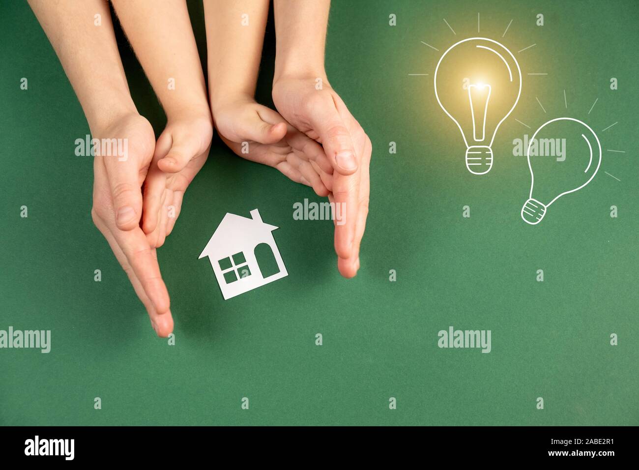 Accueil de la famille et de l'immobilier concept. Close up de femme et enfant hands holding white paper house et l'ampoule électrique image sur fond vert. Mise à plat, Banque D'Images