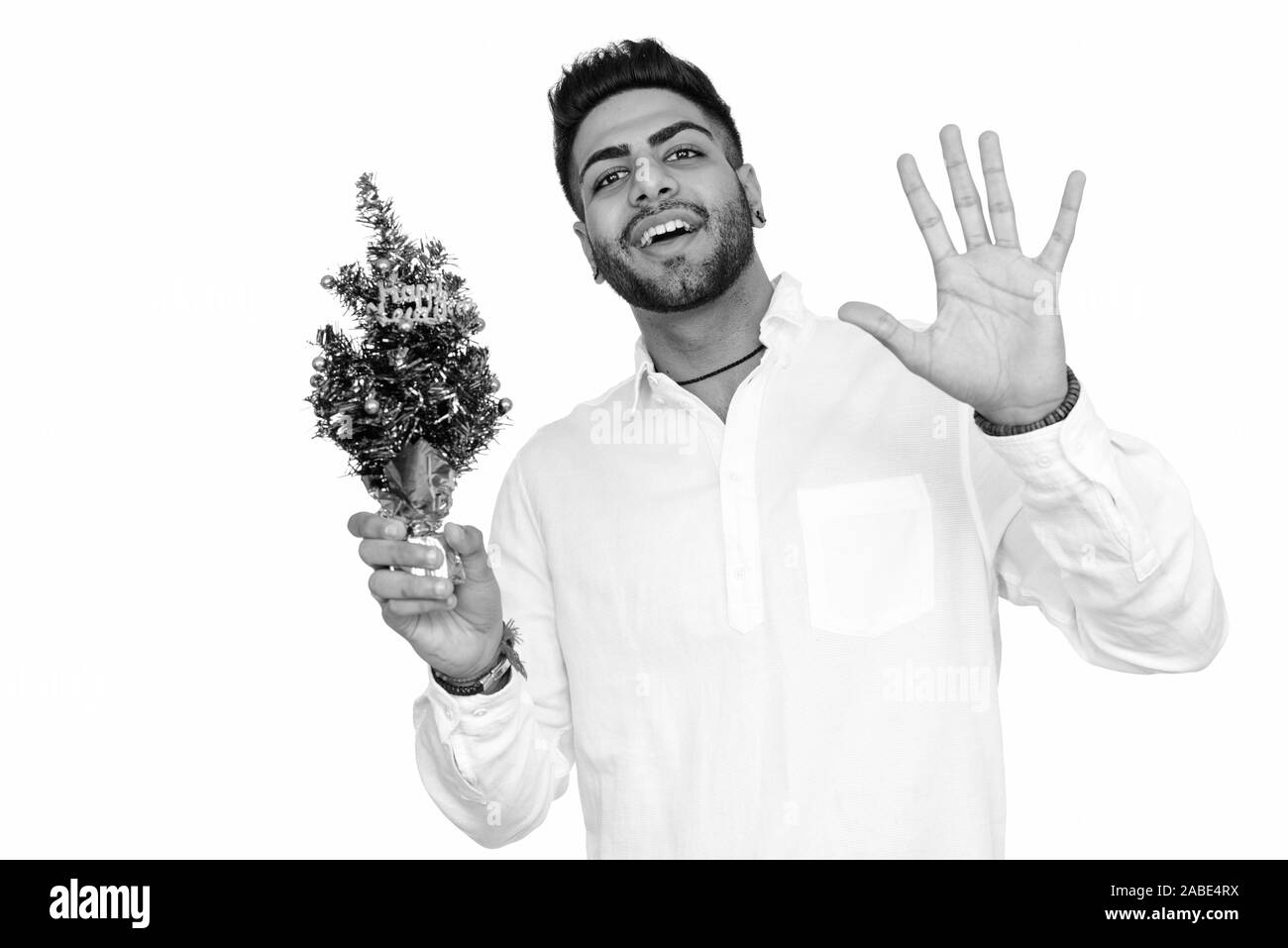 Studio shot of young happy Indian man à la surprise tout en maintenant une bonne année tree isolés contre fond blanc Banque D'Images