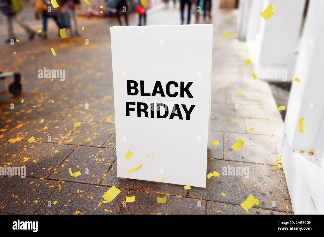 Le vendredi noir panneau publicitaire sur le trottoir de la ville, entouré de confettis et de feuilles. Les gens et shop en arrière-plan. Banque D'Images
