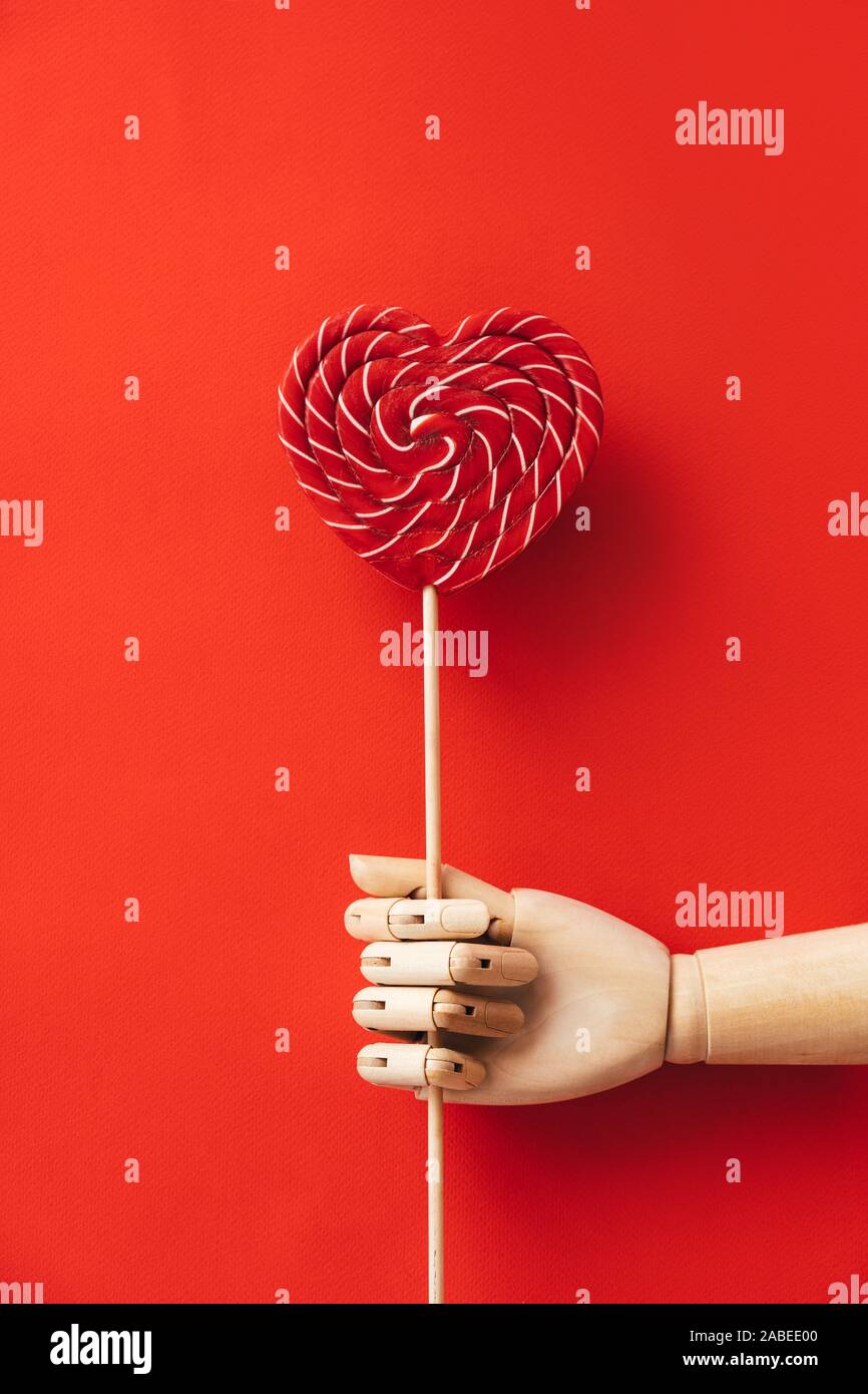 Main en bois en forme de coeur rouge et tenant un grand blanc à rayures lollipop Banque D'Images