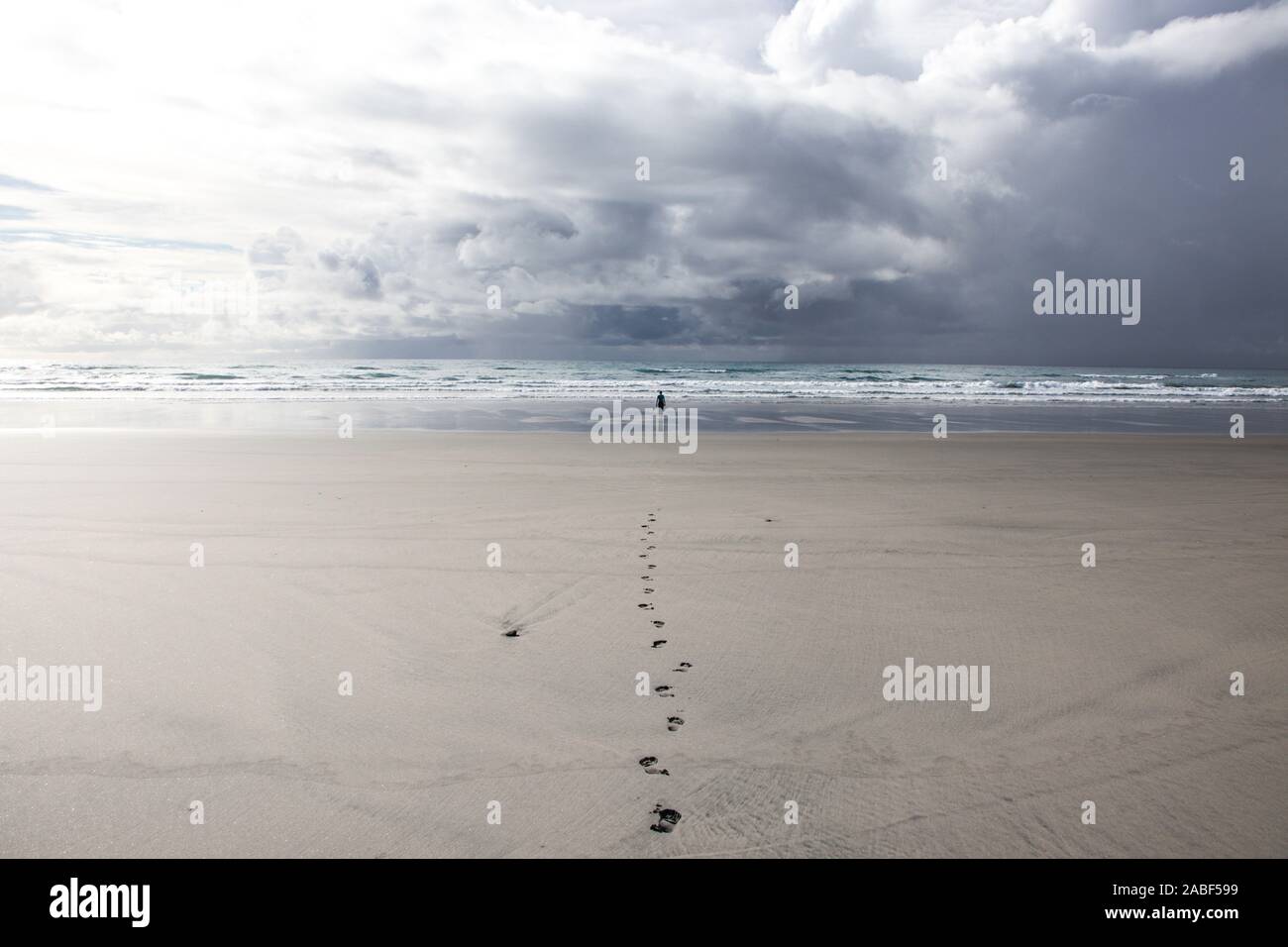 Femme en distance debout contre l'état de la mer sur la plage de très longue sous ciel nuageux spectaculaires avec une route droite des empreintes de pas menant à elle. Combustibles PVE Banque D'Images