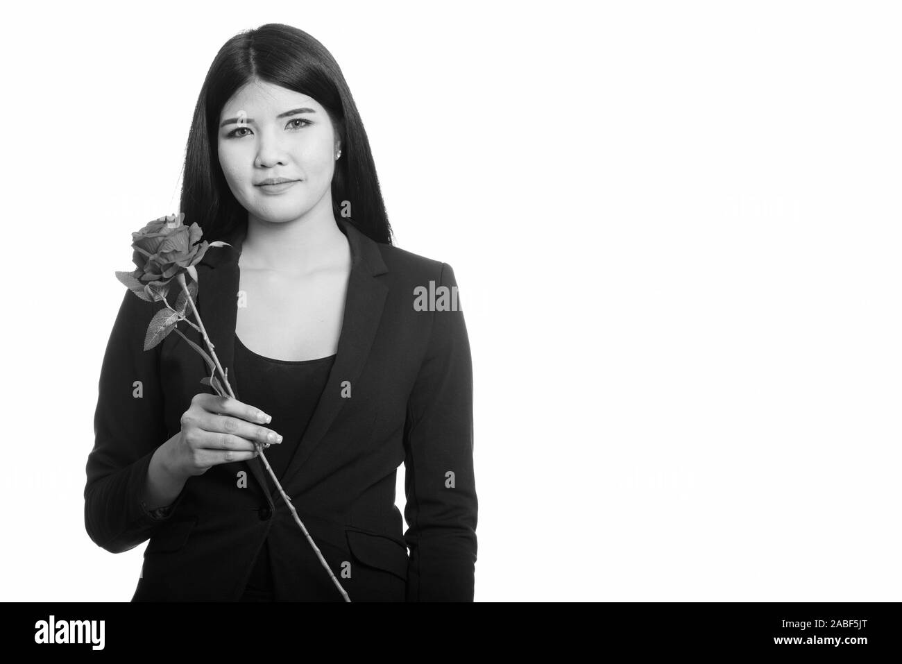 Studio shot of young beautiful Asian businesswoman holding red rose Banque D'Images
