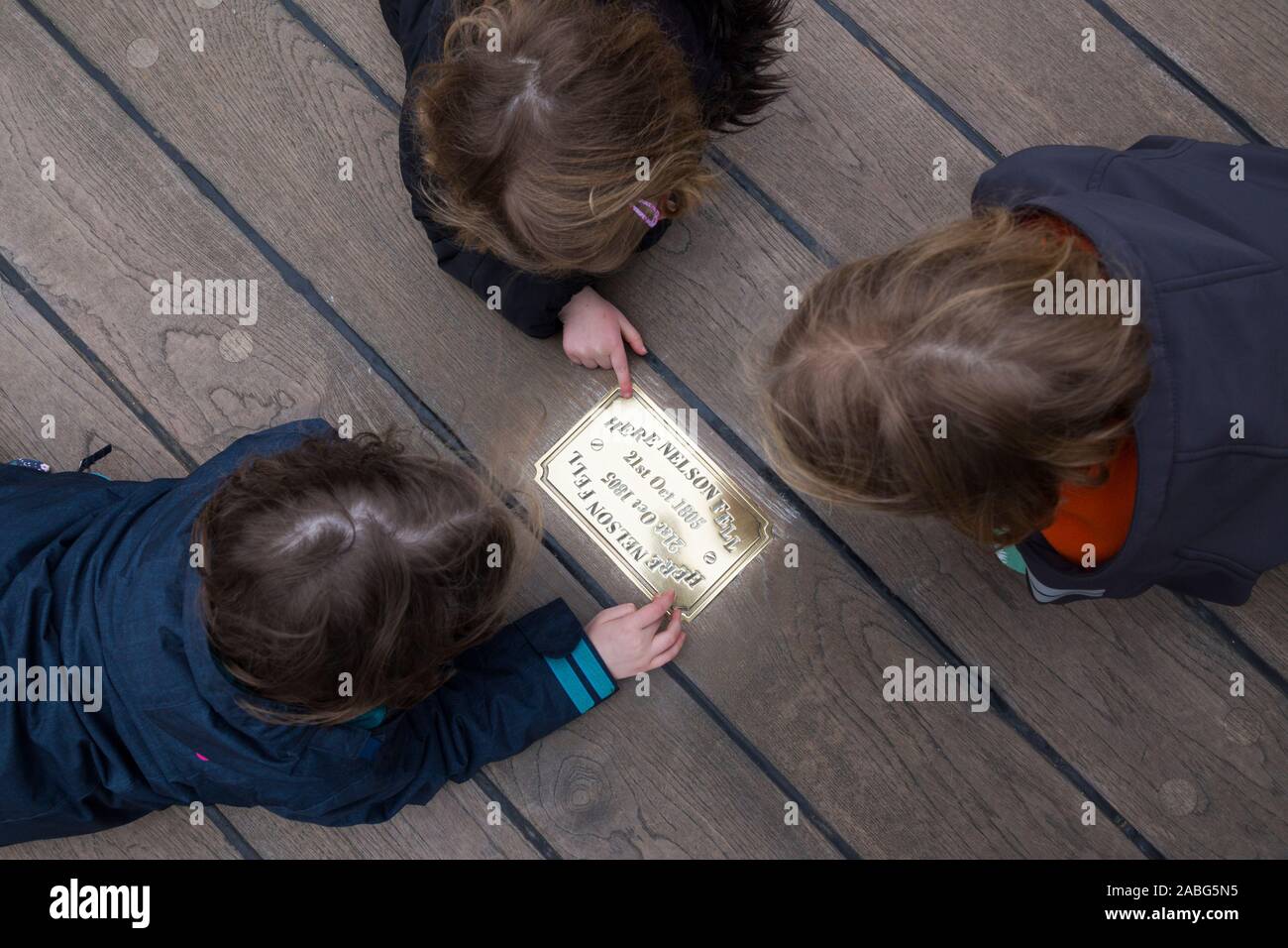 Visiteurs / touristes examiner la plaque de cuivre métallique sur le site de HMS Victory à l'endroit où l'Amiral Lord Nelson est tombé après avoir été abattu par un Mousquetaire français. Portsmouth. Royaume-uni (105) Banque D'Images