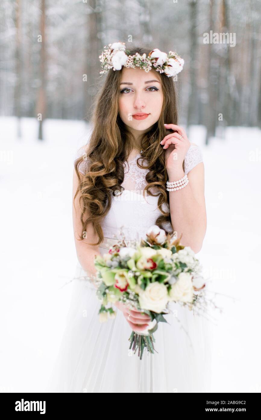 Belle Mariée. Mariage d'hiver. Jeune femme en robe de mariage avec une  couronne de fleurs en coton et le bouquet debout dans la forêt d'hiver et à  la Photo Stock - Alamy