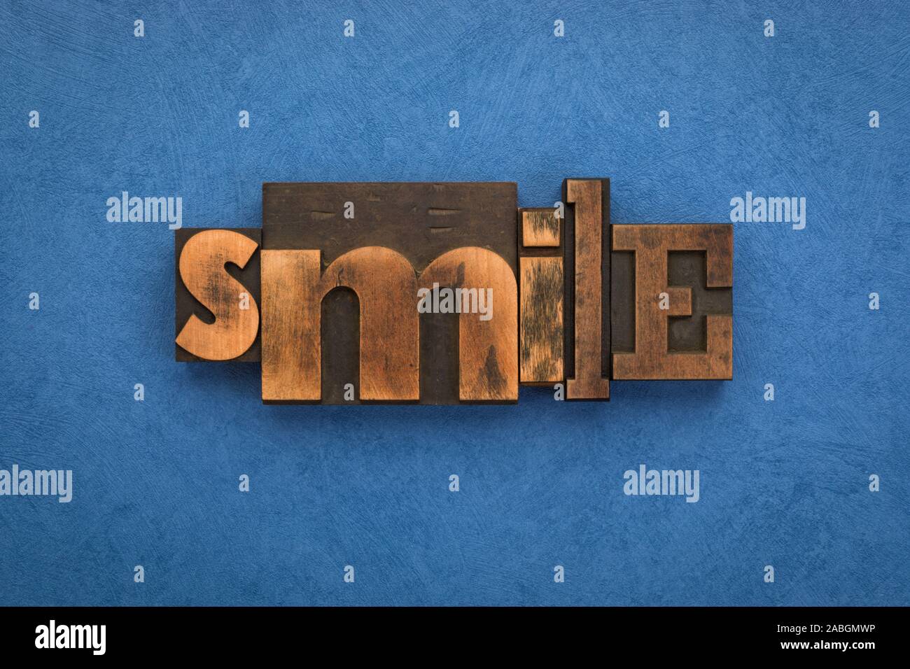 Sourire, seul mot écrit avec la typographie vintage blocks sur fond bleu texturé. Banque D'Images