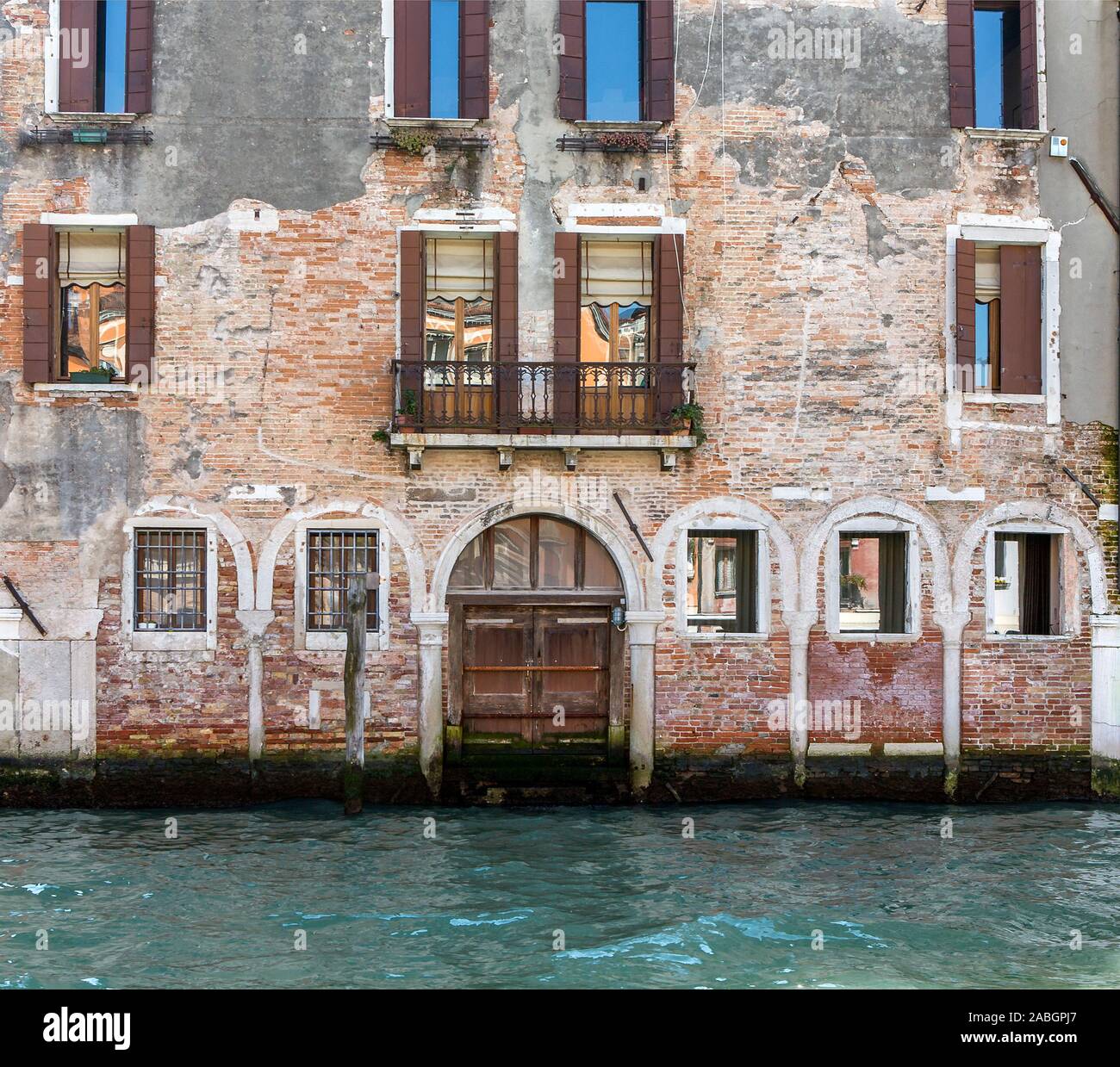 Vue partielle de vieux bâtiment abandonné face à Grand Canal à Venise, Italie. Vieilles briques, fenêtres, porte fermée, l'eau. Banque D'Images