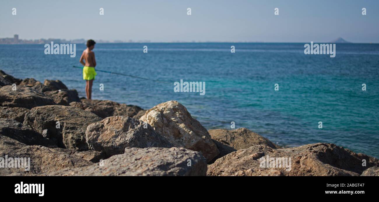 Une personne seule, pêchant au large d'un brise-lames rocheux, un jour d'été ensoleillé en Méditerranée Banque D'Images