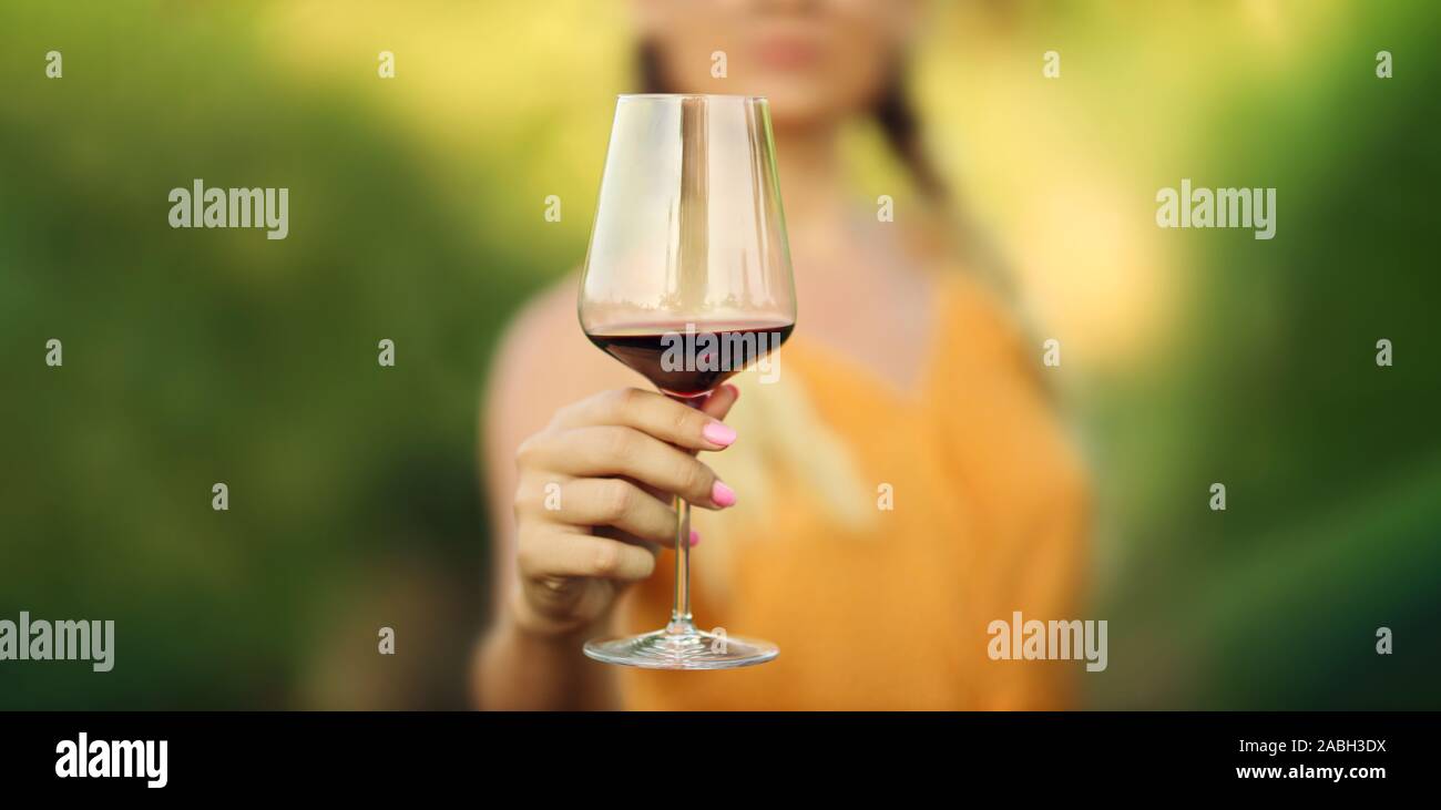 Femme main tenant un verre de vin rouge. Se concentrer sur le verre de vin. Verre de vin rouge avec des femmes. Vignoble floue fond. Copier l'espace. Banque D'Images