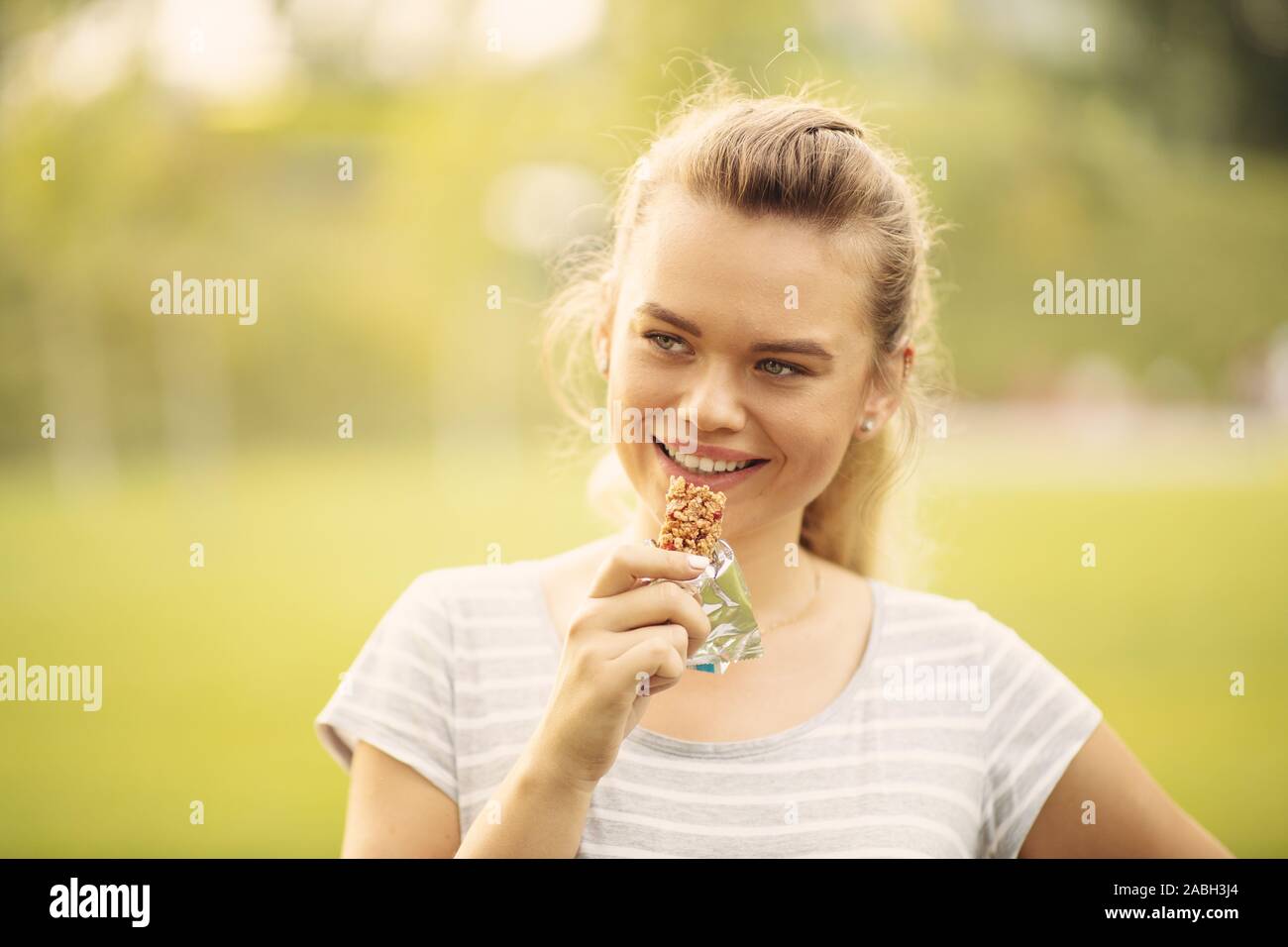 Femme mangeant une barre de protéines après l'entraînement en plein air - libre face of young blonde woman sportive tout en mordant un barre nutritive Banque D'Images