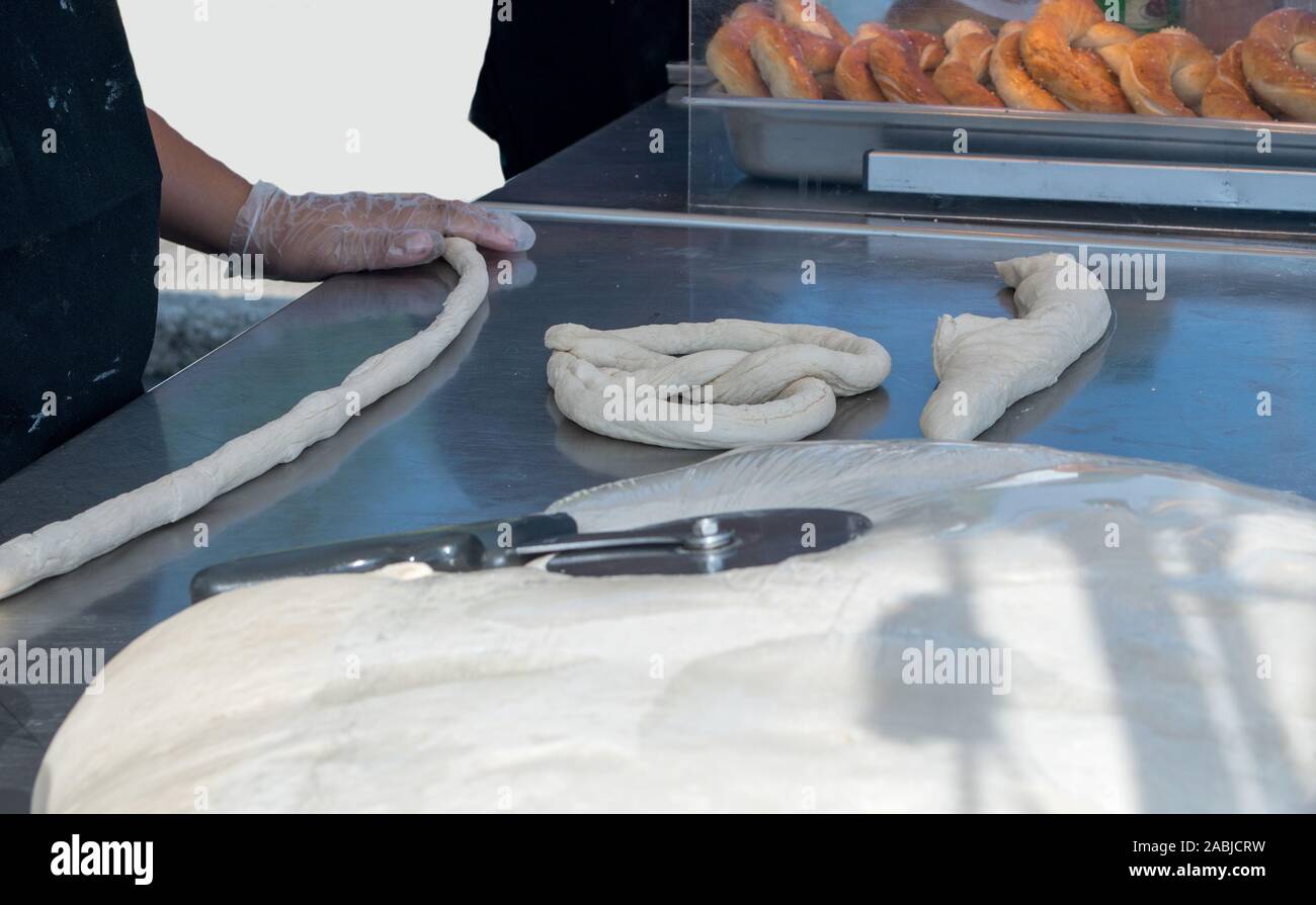 Les rouleaux d'un boulanger pâte crue dans une corde pour faire un bain, des bretzels frais du four Banque D'Images