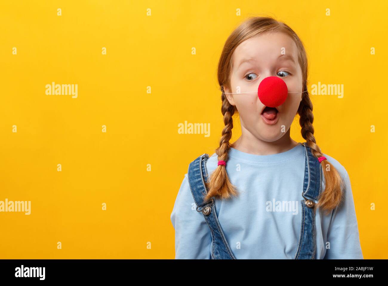 Clown enfant drôle avec un nez rouge. Petite fille joyeuse sur un fond jaune. 1er avril Fool's Day. L'espace de copie, Banque D'Images