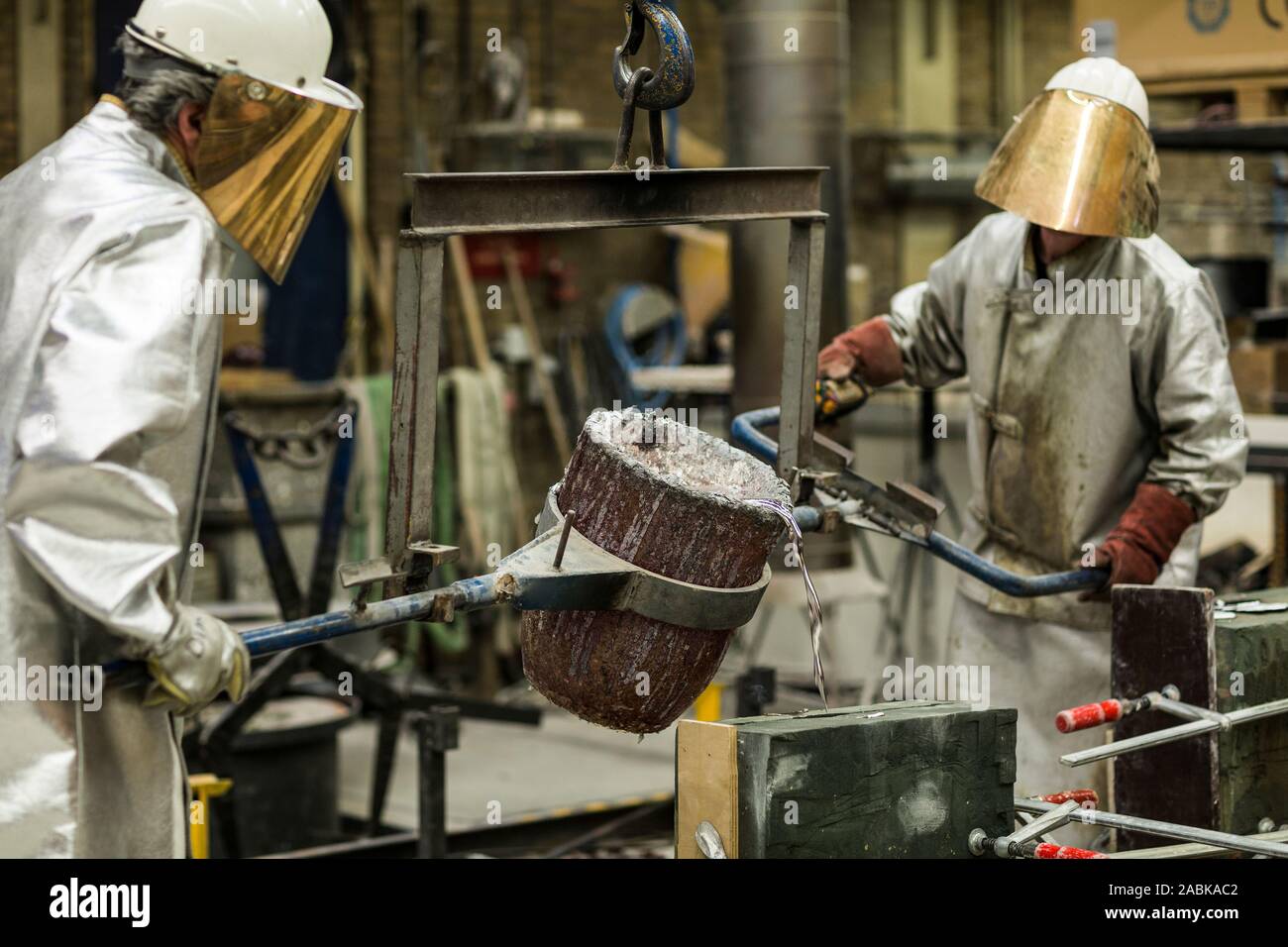 Deux artisans dans des vêtements d'argent au sable faire technique de coulage de l'aluminium en fusion liquide de couleur argent dans un moule dans un induastr Banque D'Images