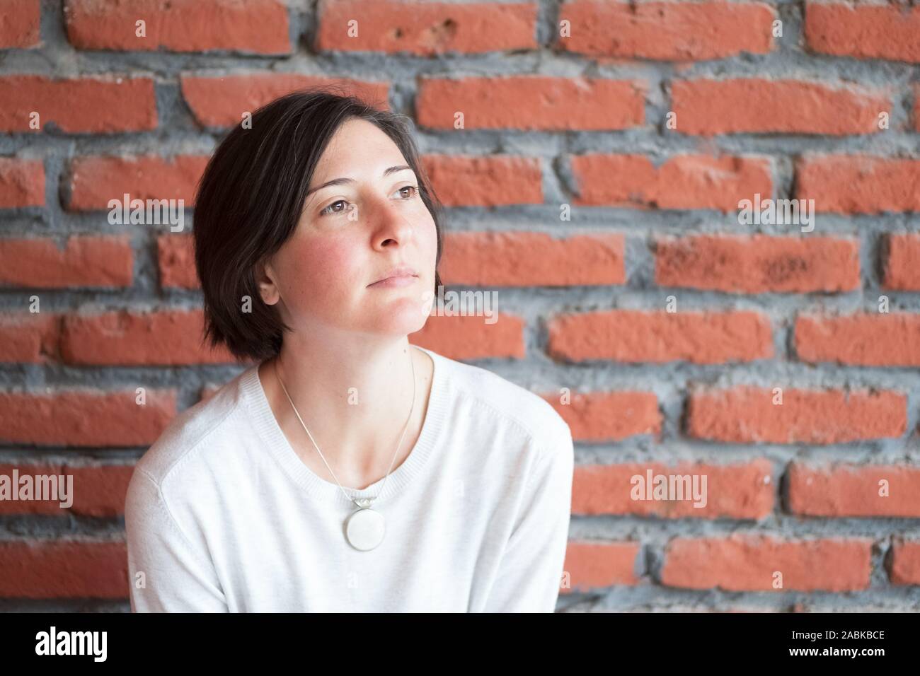 Portrait d'un adulte femme brune avec des cheveux bruns courts dans des vêtements décontractés, debout devant un mur de briques. Banque D'Images