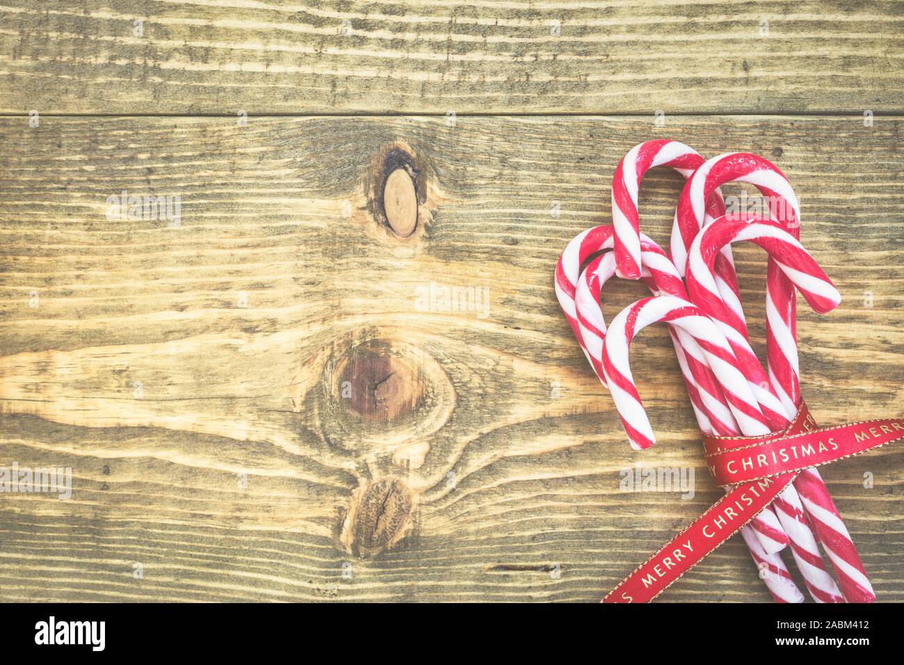 Des cannes de bonbon enveloppé de ruban rouge de Noël sur fond de bois. Tons vintage photo. Vue supérieure avec copie espace sur le côté gauche. Banque D'Images