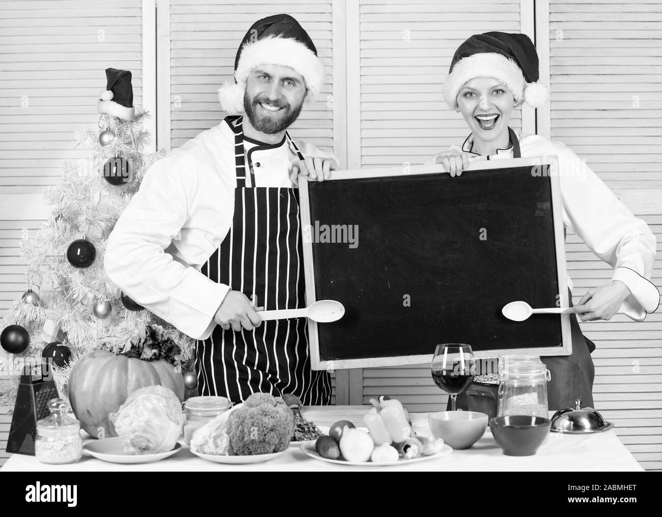 L'homme et la femme chef santa hat near Christmas Tree tenir copie tableau noir l'espace. Menu traditionnel de la famille pour le dîner de Noël. Menu pour notre famille. Recette de Noël concept. La cuisson des repas de Noël. Banque D'Images